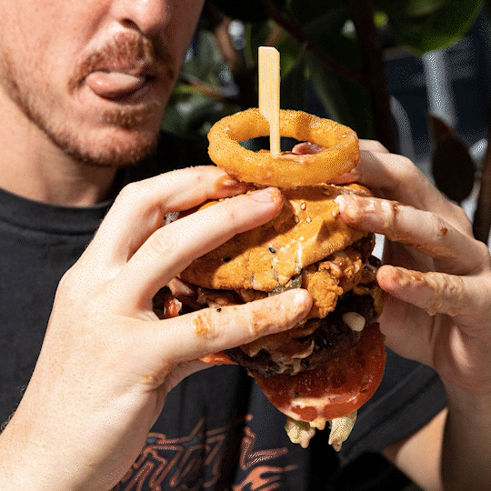 Person holding a large burger with fried chicken, onion ring, tomato, and lettuce.
