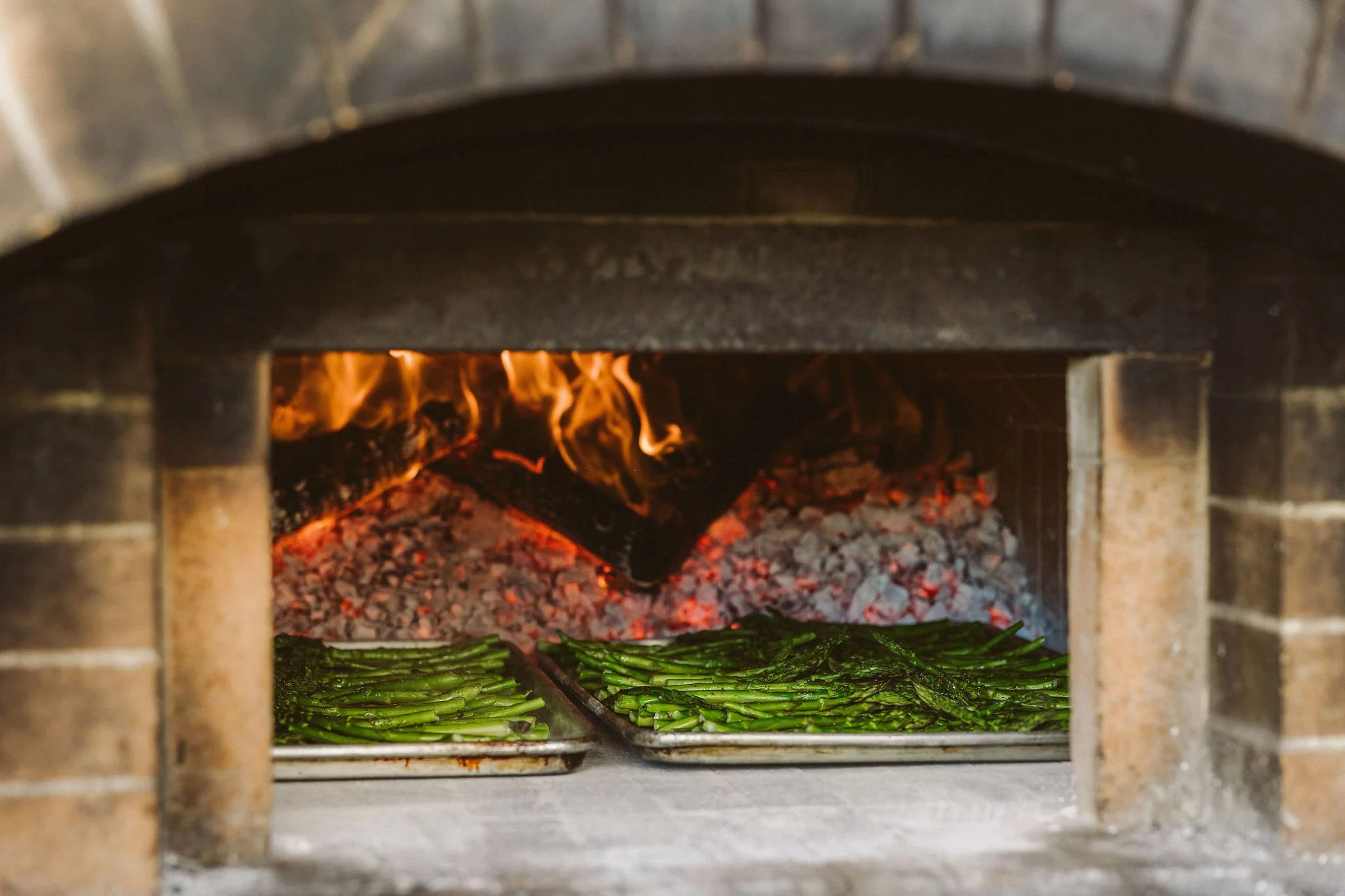 Cooking asparagus in a brick oven with flames and hot coals.