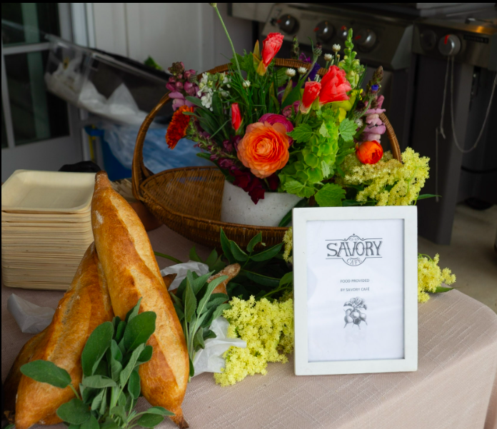 Fresh baked bread, a floral arrangement of pink and green flowers, and a framed sign on a table in a dining area.
