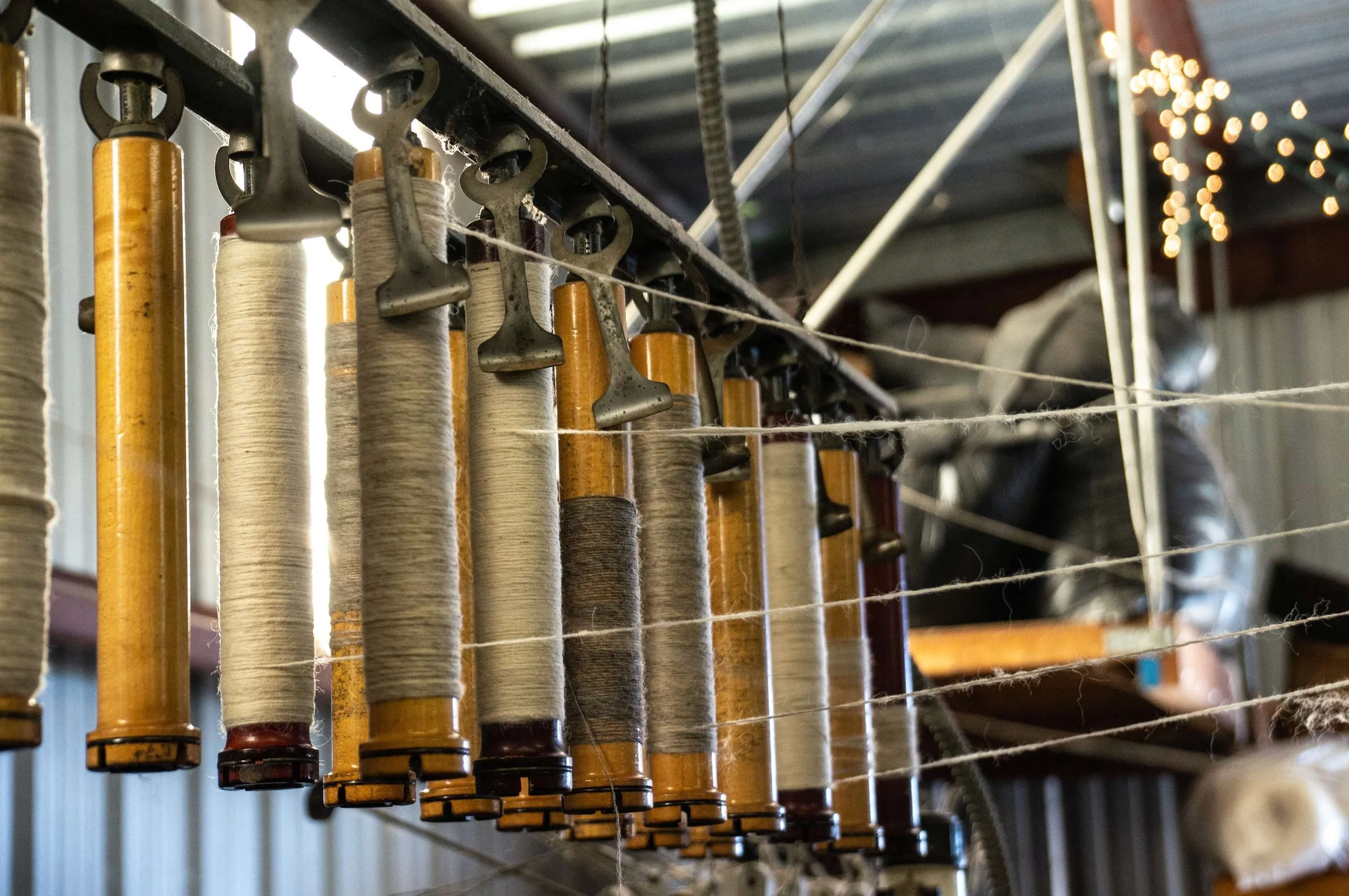 Multiple textile spools hanging from a metal rack in a workshop.
