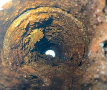 Looking down into a rusty, corroded pipe with light visible at the end.