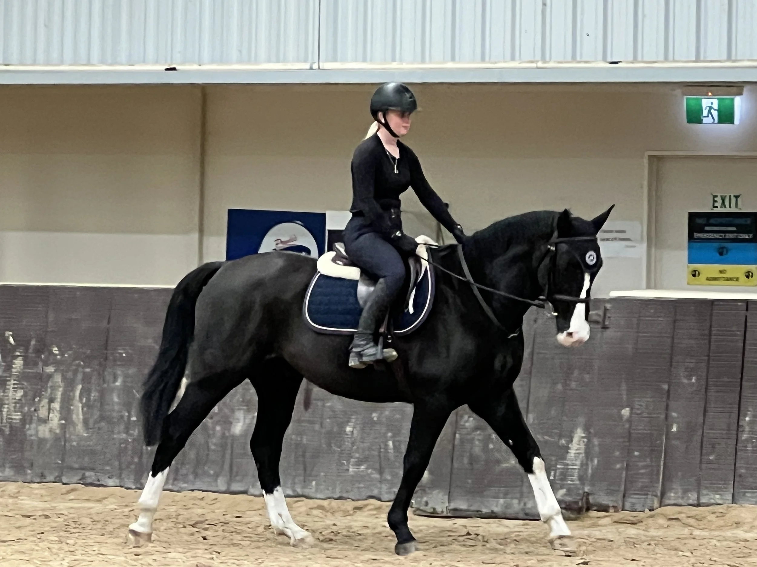 A person riding a black horse with white markings in an indoor riding arena.