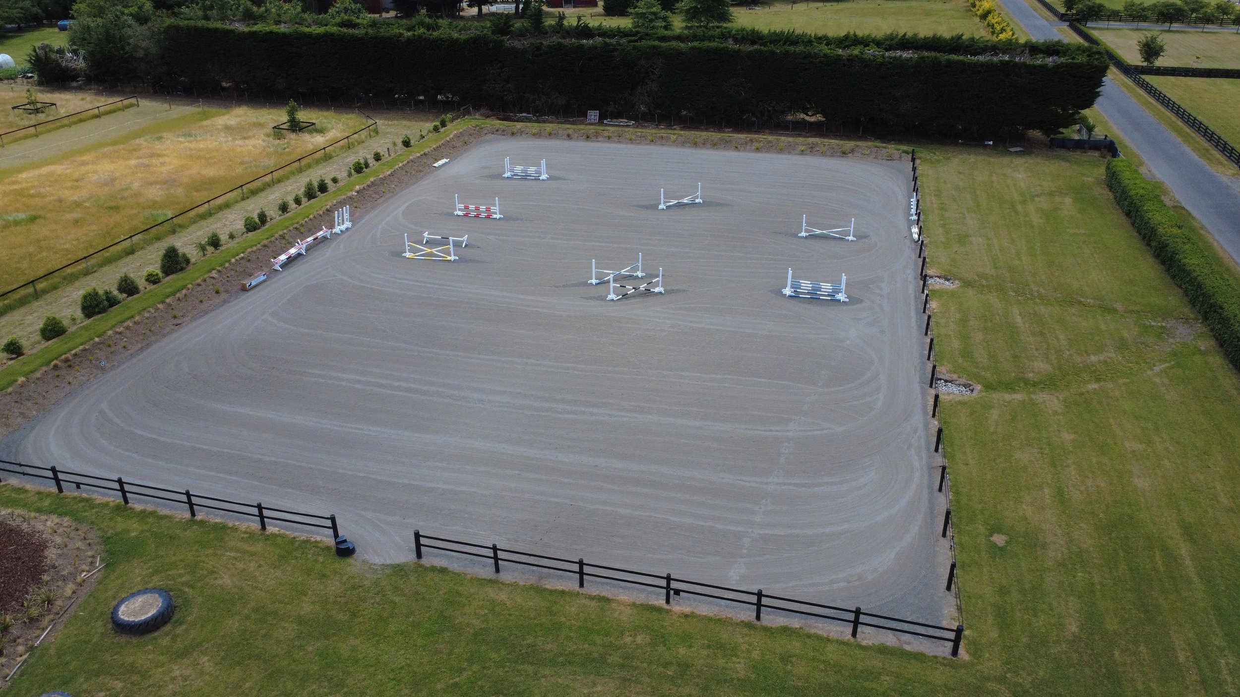 An outdoor equestrian jumping arena with several jumps set up for horse training, surrounded by grassy areas and fencing.