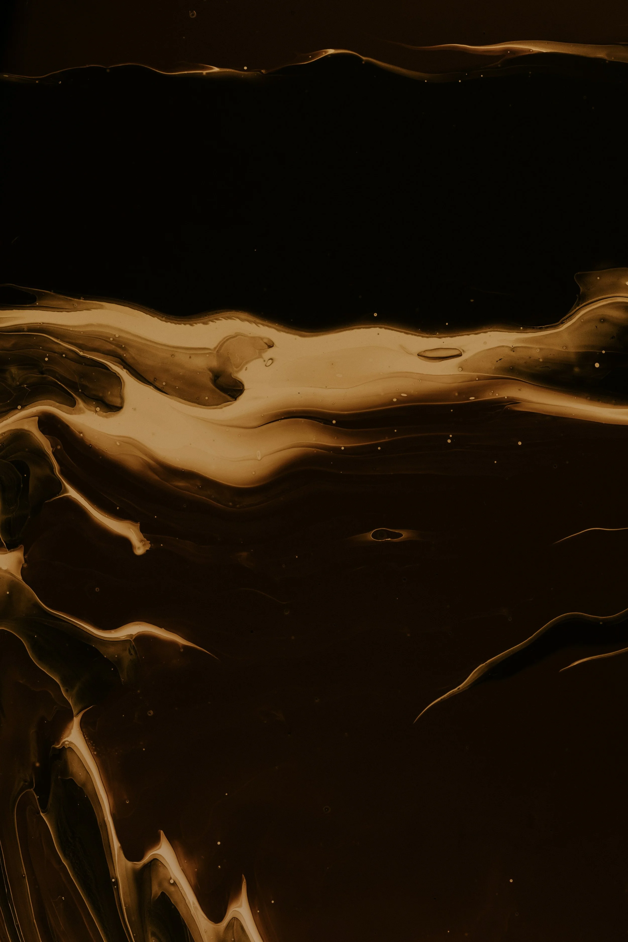 Abstract image of swirling dark brown and beige liquid with flowing patterns and small bubbles.