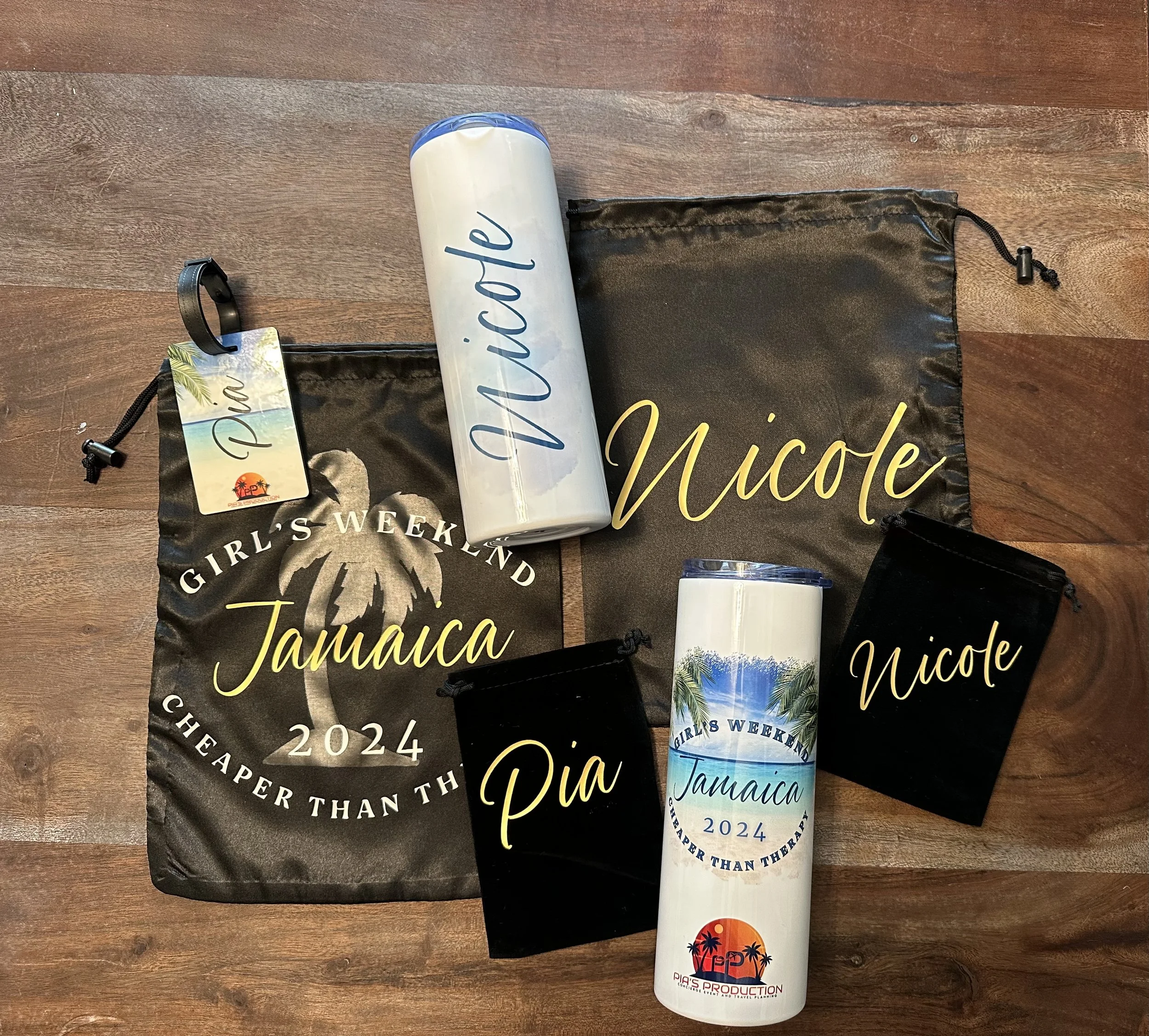 Travel accessories and personalized items for Nicole and Pia, including two black drawstring bags, two white water bottles with a tropical Jamaica theme, and two small black pouches, all laid out on a wooden surface.