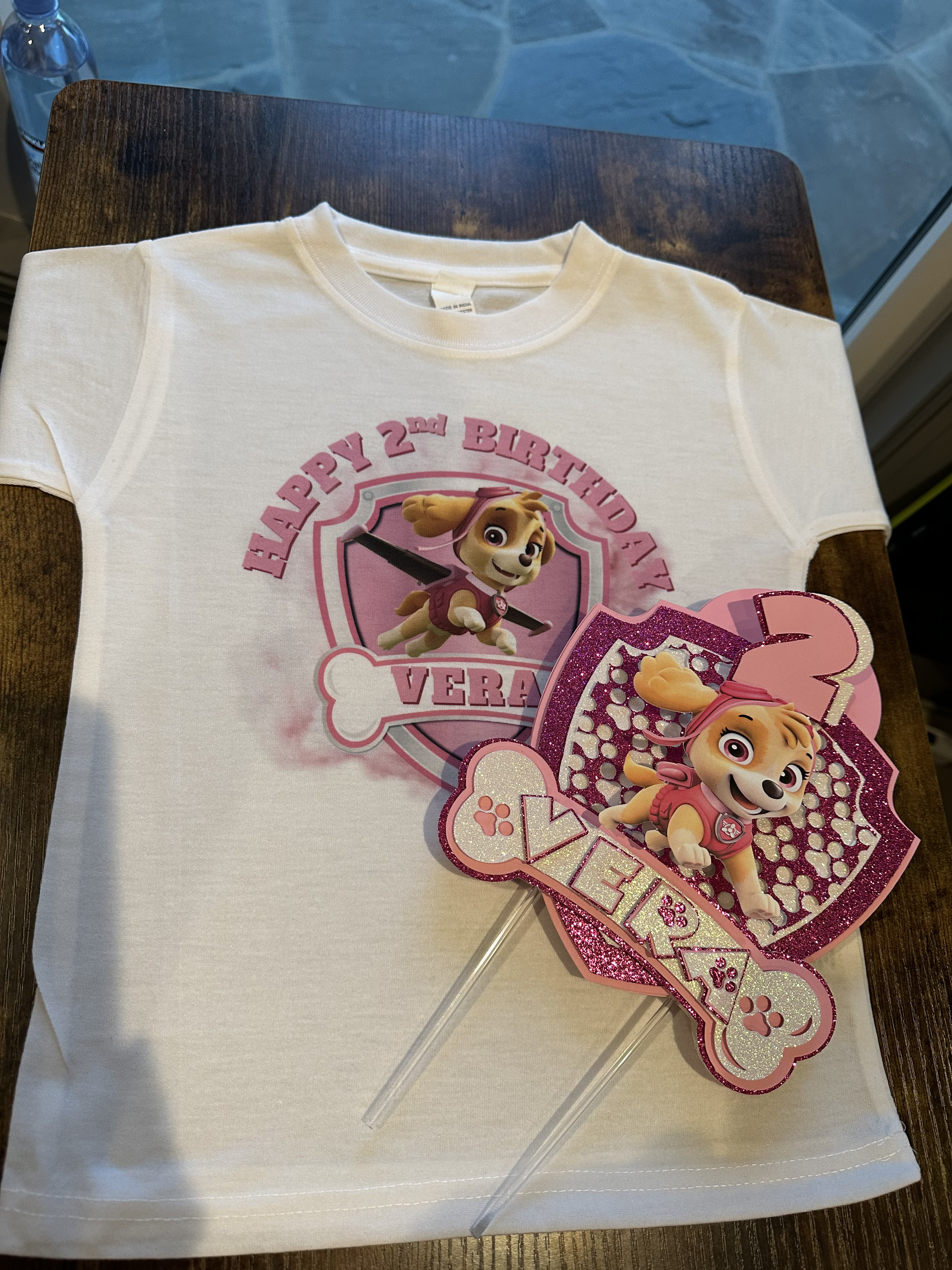 A white t-shirt and a birthday cake topper with a cartoon puppy from Paw Patrol, celebrating a second birthday.