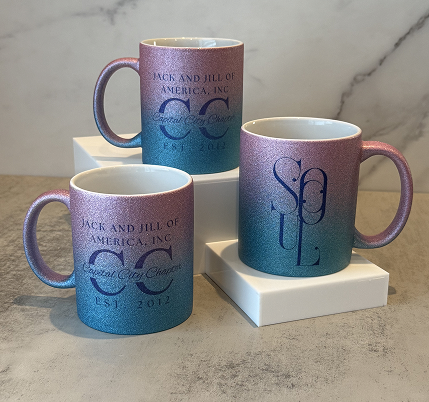 Three gradient-colored mugs with blue and purple hues featuring the words "Jack and Jill of America, Inc." and logos, placed on white stands on a marble-like surface.
