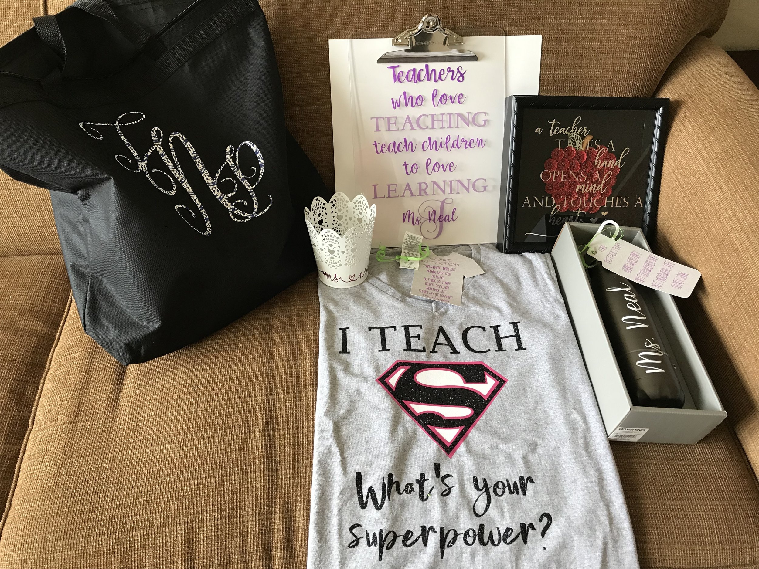 Various teacher-themed items including a black gift bag with a rhinestone script, a white clipboard with purple text, a framed quote with red roses, a white box with black lettering, a gray t-shirt with Superman logo and text, and a white paper cup w