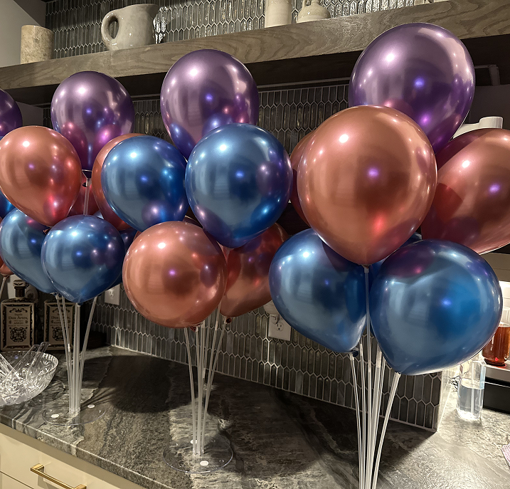 Multiple metallic balloons in shades of purple, blue, and copper arranged on a kitchen countertop.