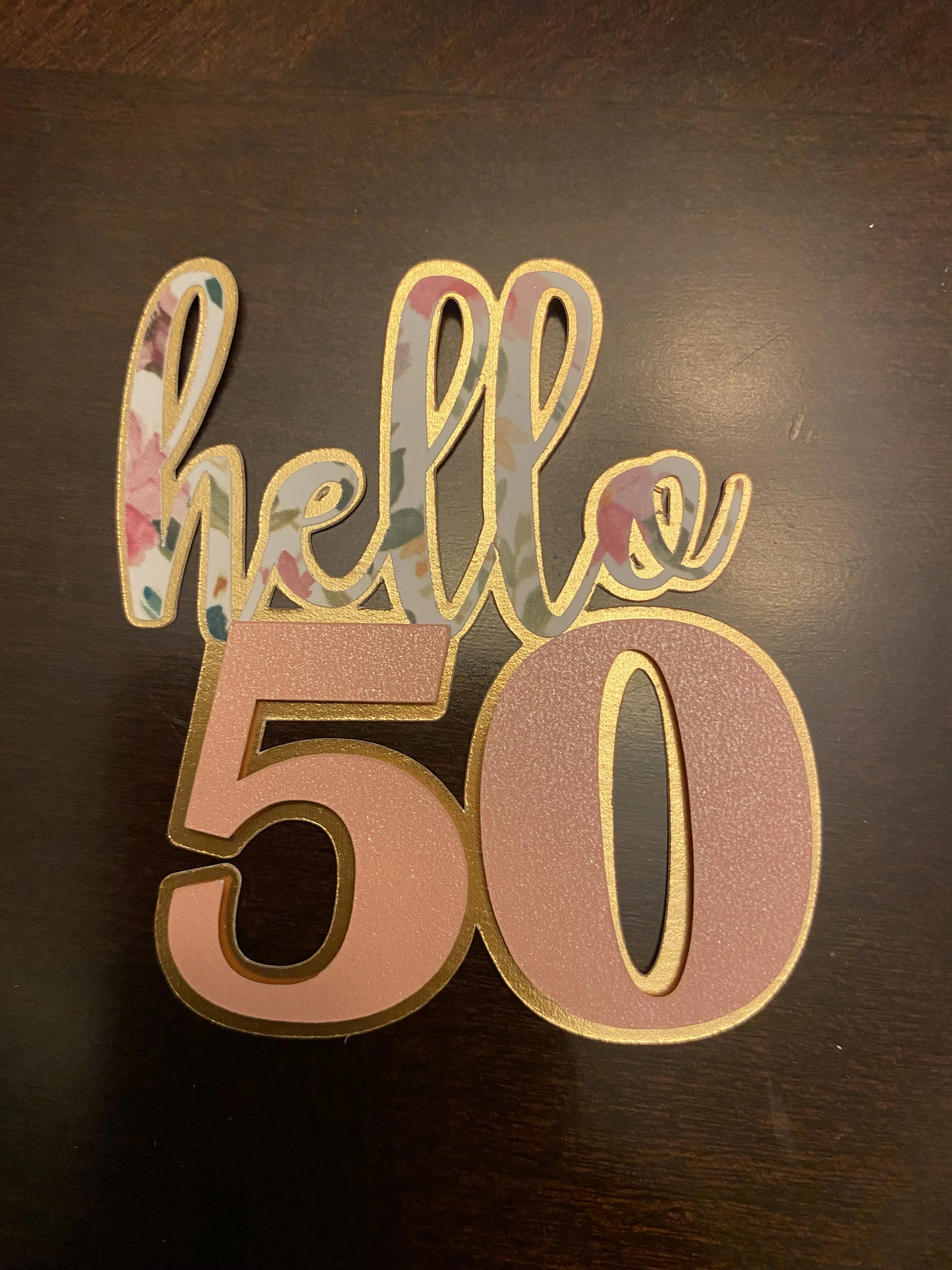 Decorative sign that says 'hello 50' in pink and gold colors with floral pattern.