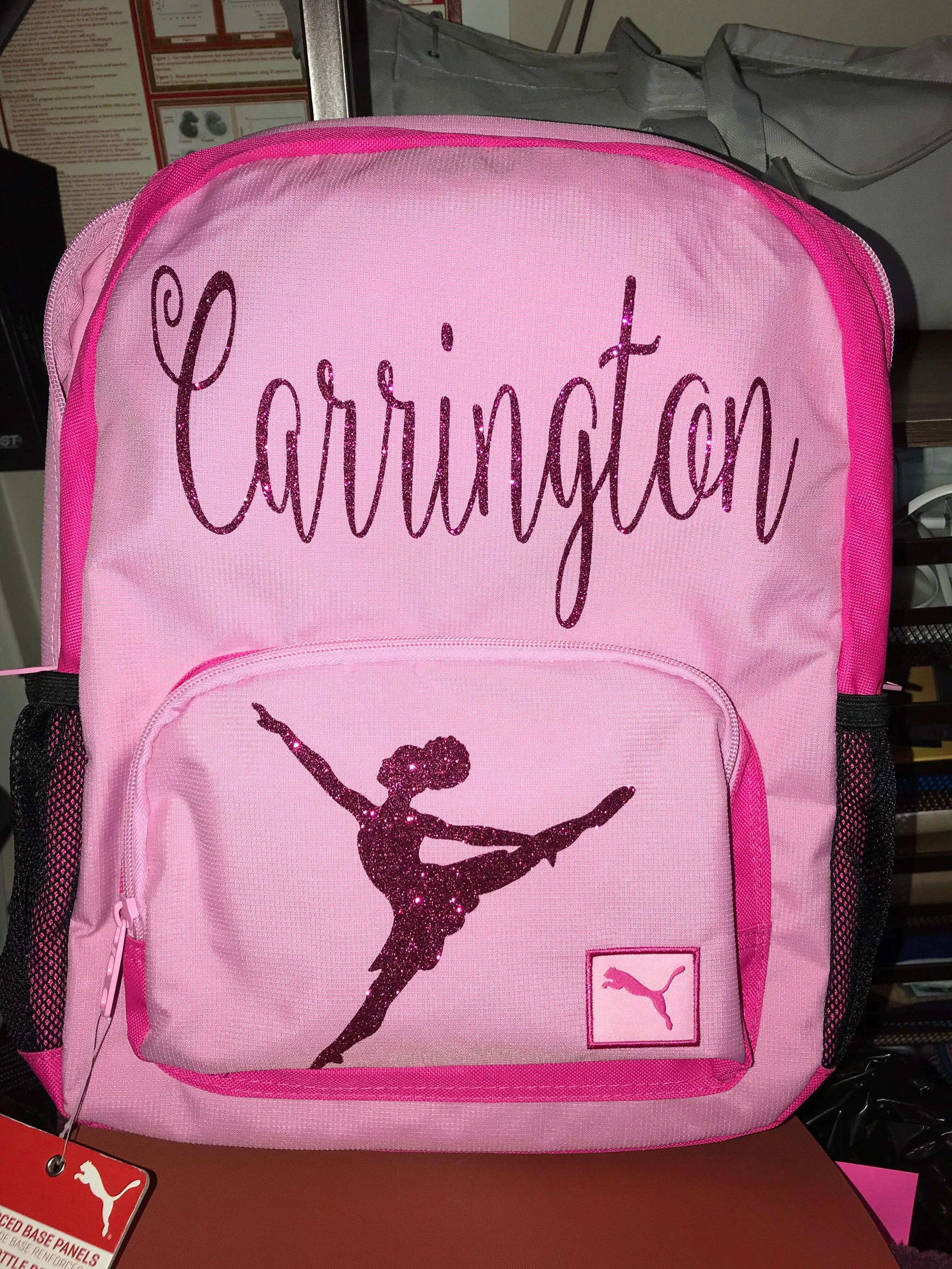 Pink backpack with the word 'Carrington' written in glittery purple on the top and a glittery silhouette of a gymnast in a pose on the front pocket.