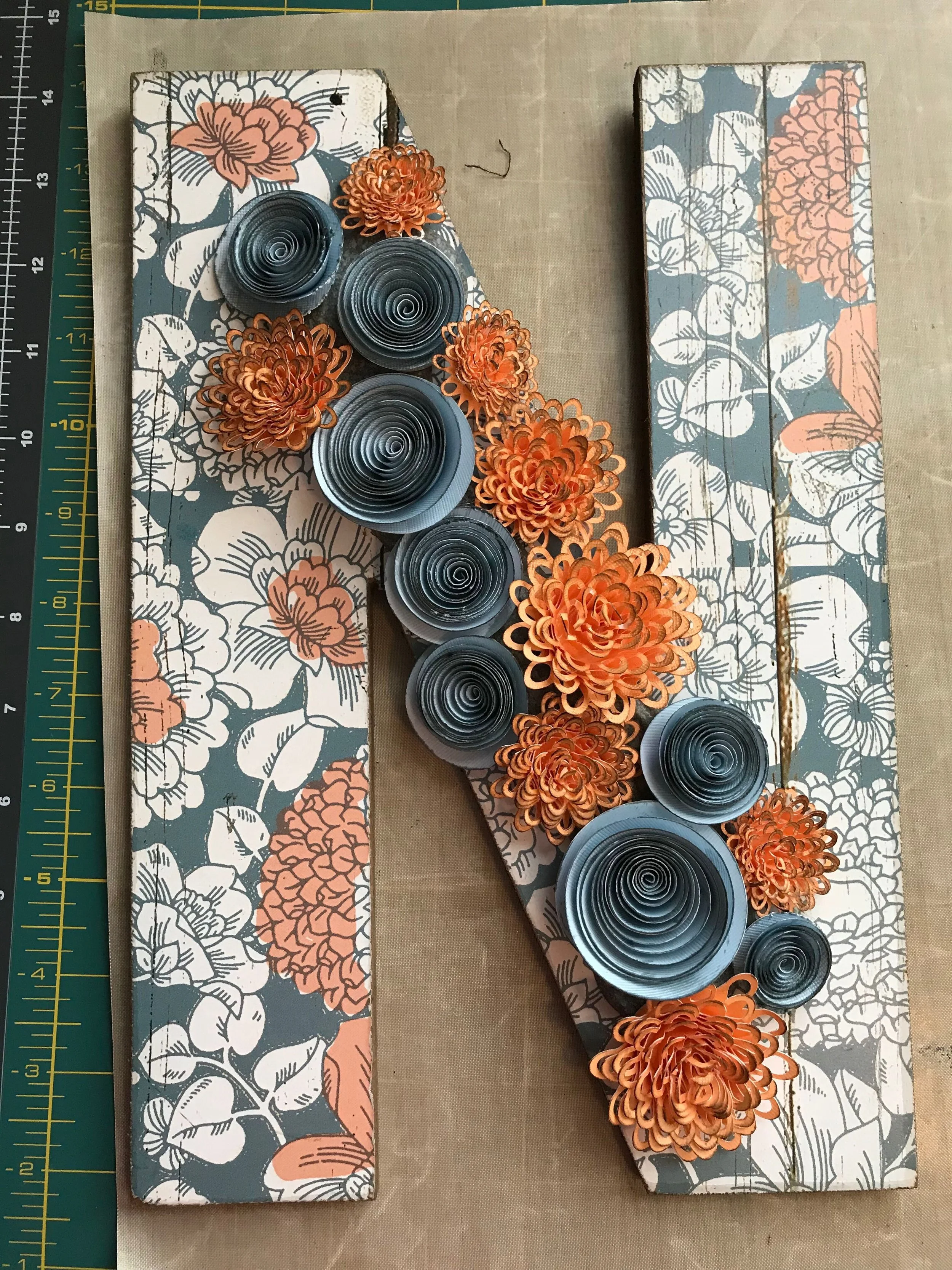 Decorative letter 'N' made from floral patterned wood, featuring orange paper flowers and black and white spiral paper art.