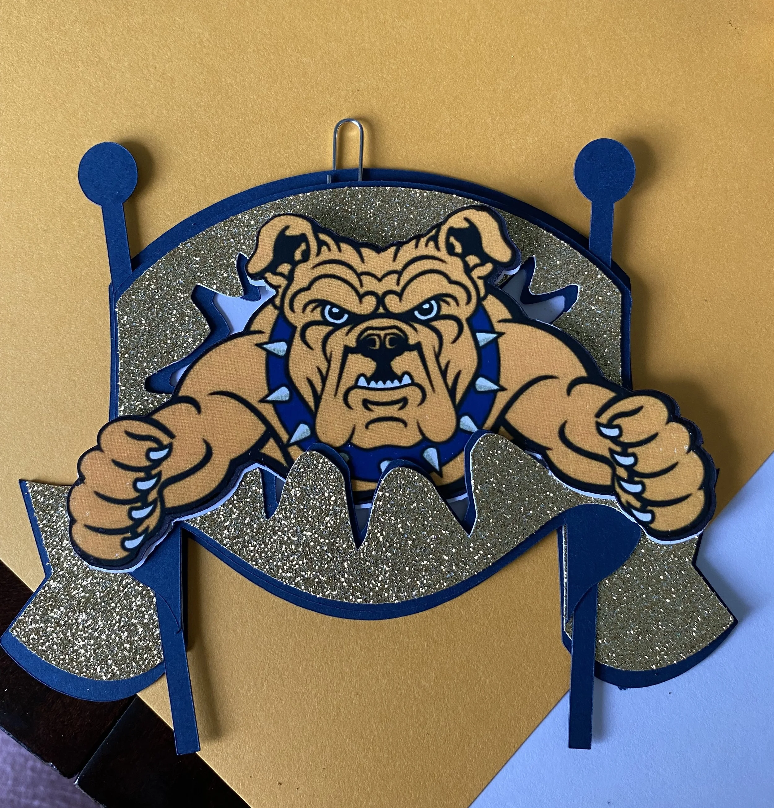 Decorative bulldog with an angry expression, surrounded by blue and gold accents, mounted on a gold and glittery background.
