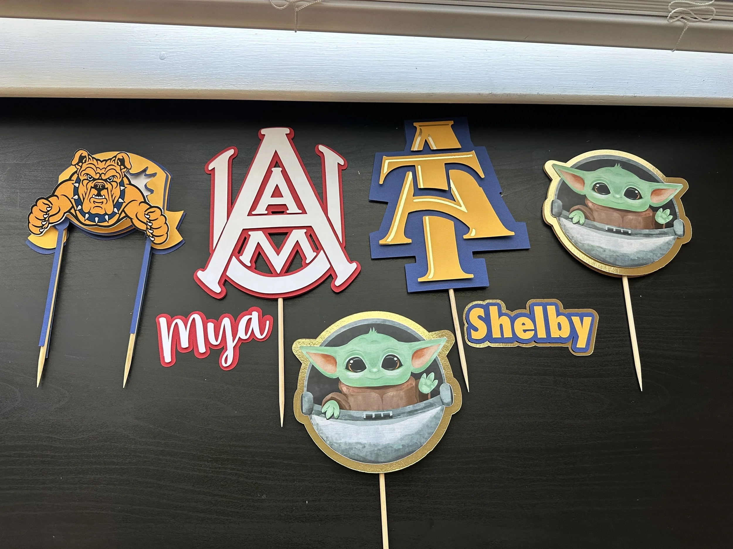 Decorative birthday toppers featuring a bulldog mascot, the University of Alabama emblem, and Grogu from Star Wars, with the name Shelley.