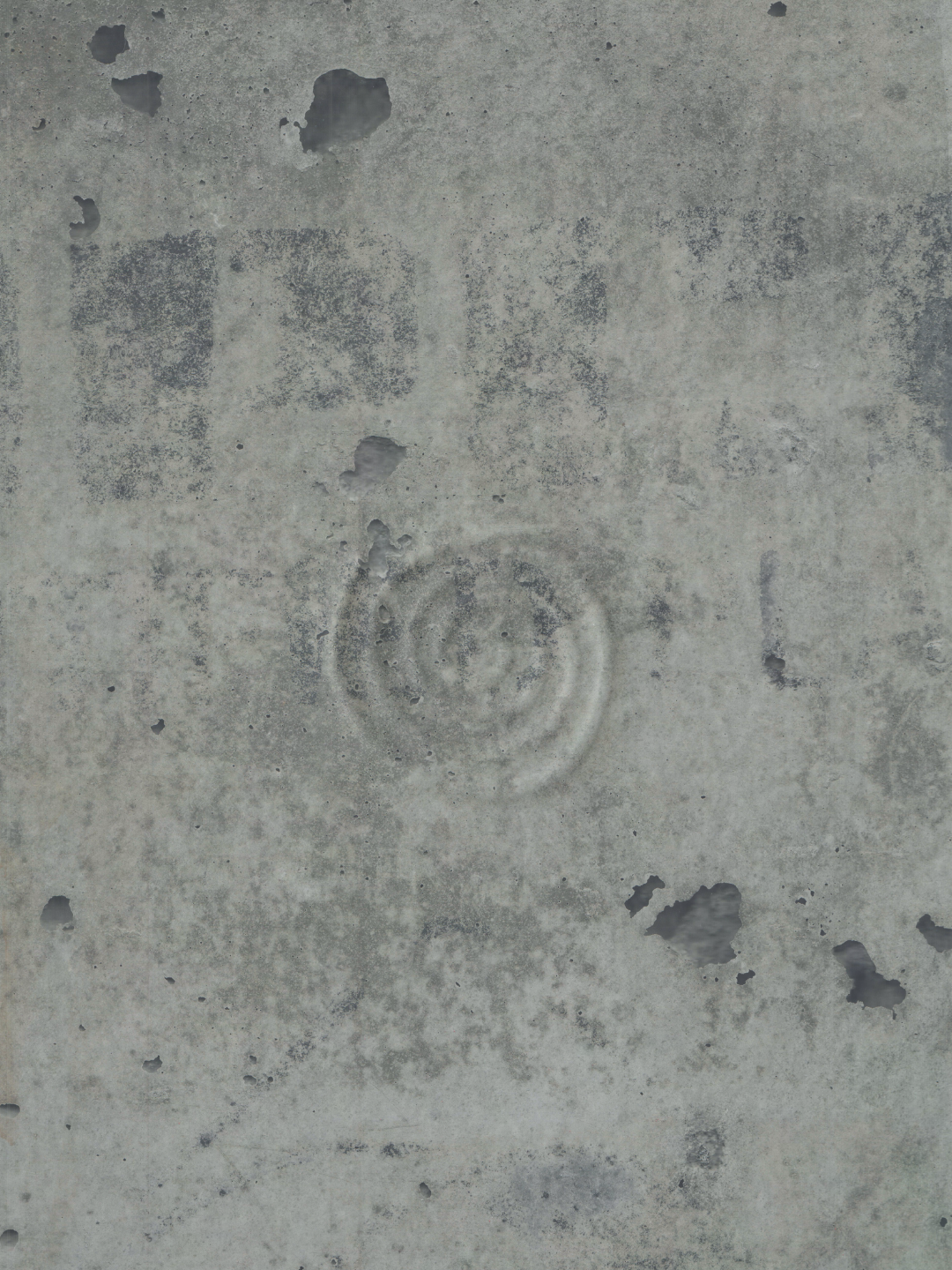 Close-up of a weathered concrete surface with holes, stains, and a faint spiral pattern.