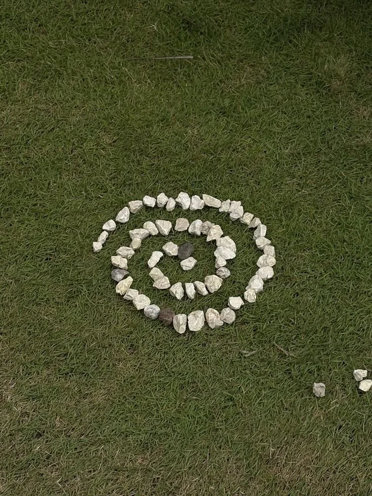 A spiral pattern made of small white and dark stones arranged on grass.