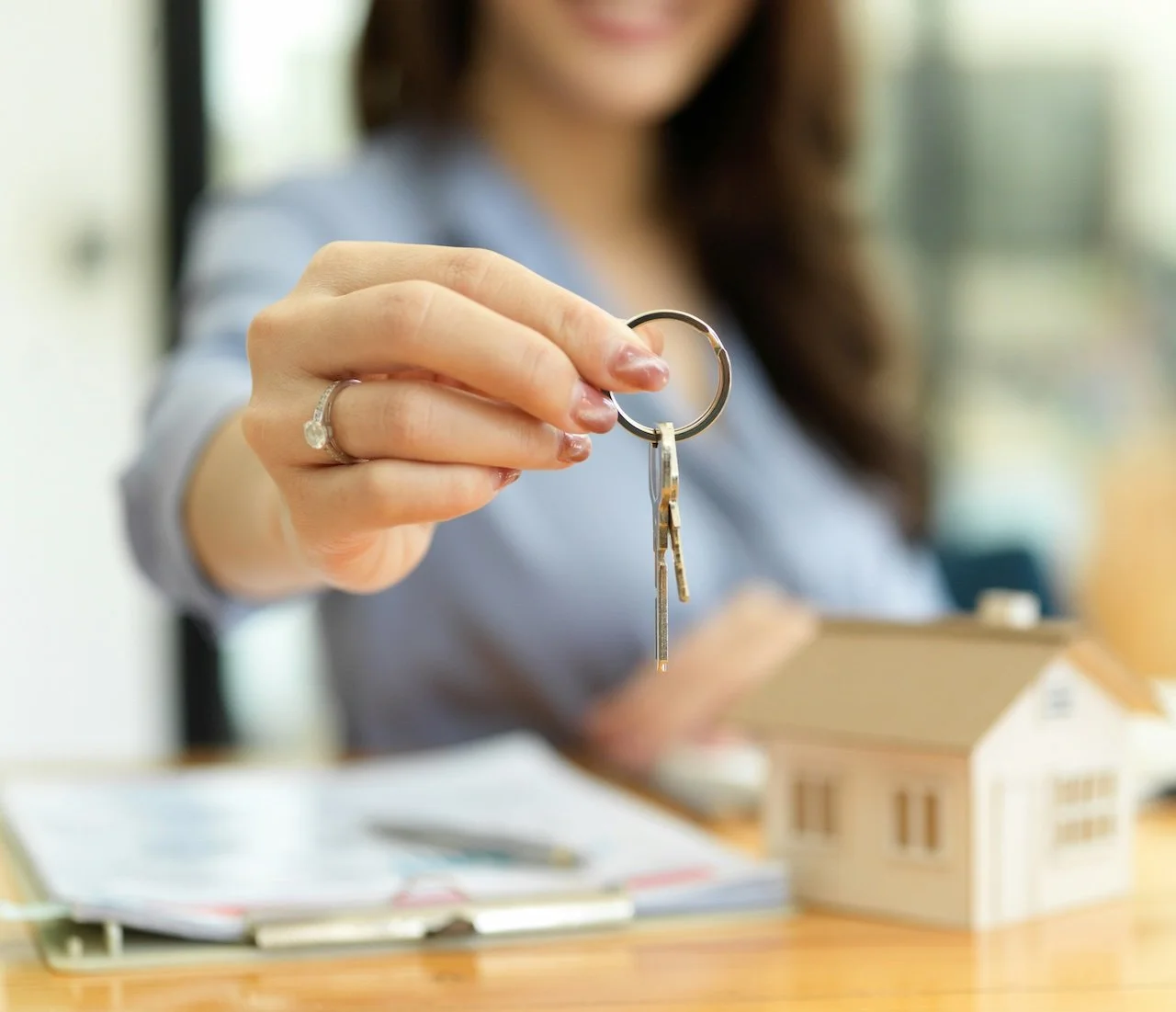 Woman holding a set of keys in front of a small model house on a table