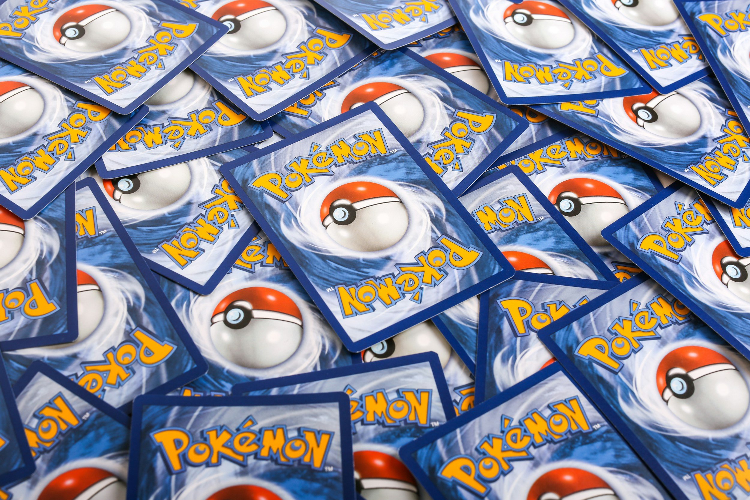 A pile of scattered Pokémon trading cards with a blue background and a Pokéball image in the center.