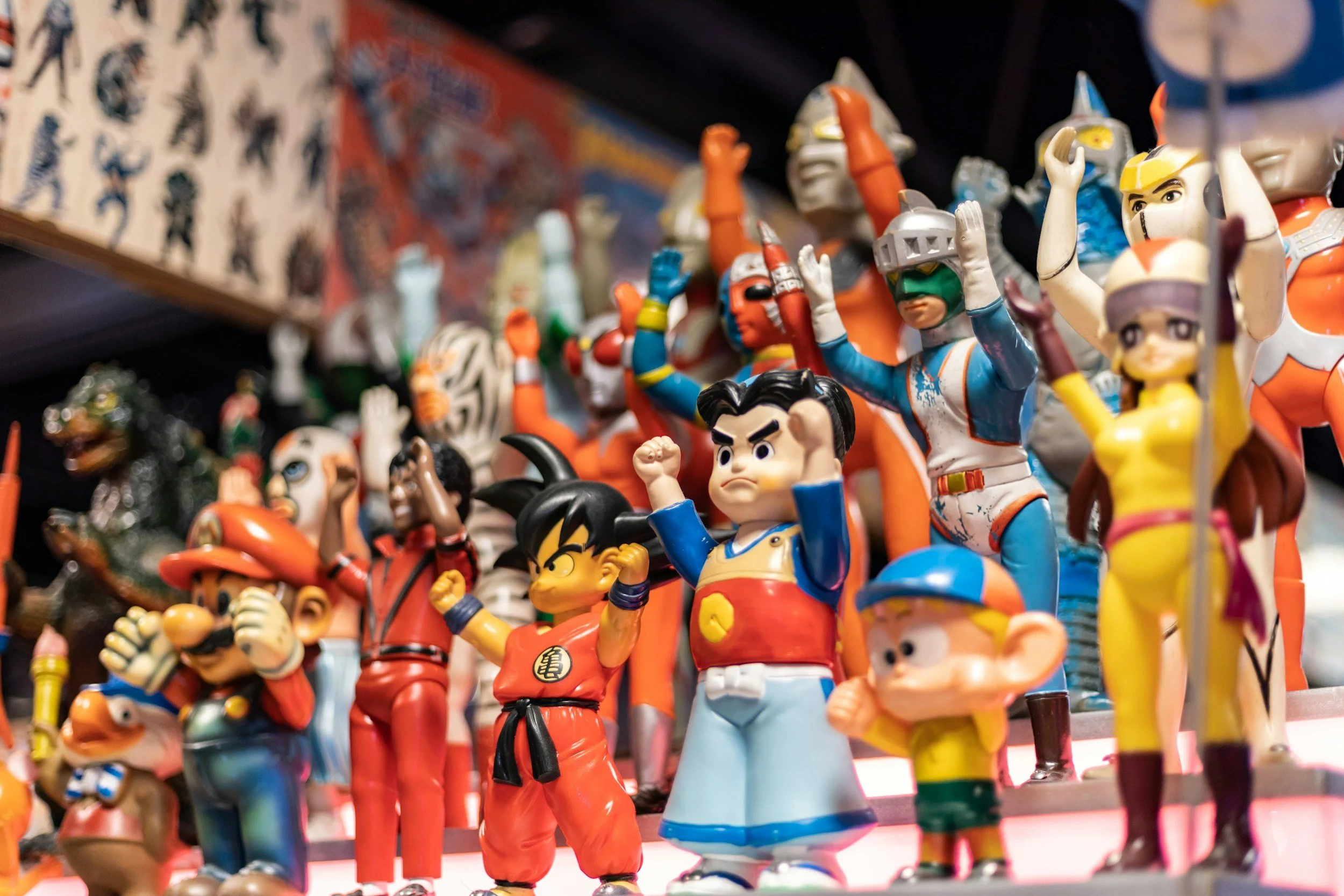 A shelf filled with colorful anime and cartoon figurines, including characters from popular shows like Dragon Ball, Super Mario, and other Japanese animations, arranged in a display.