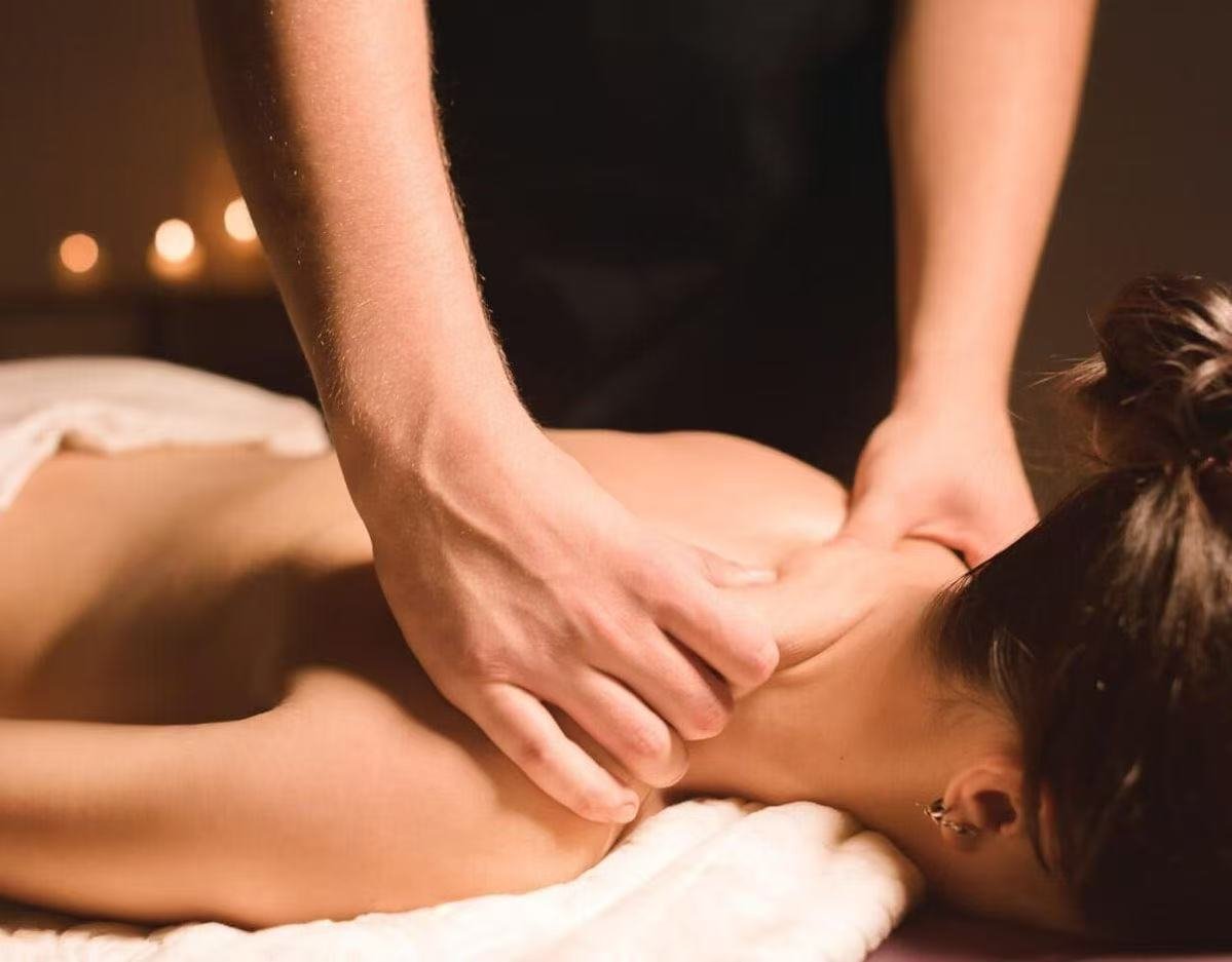 A person receiving a massage on their back in a spa setting with candles in the background.