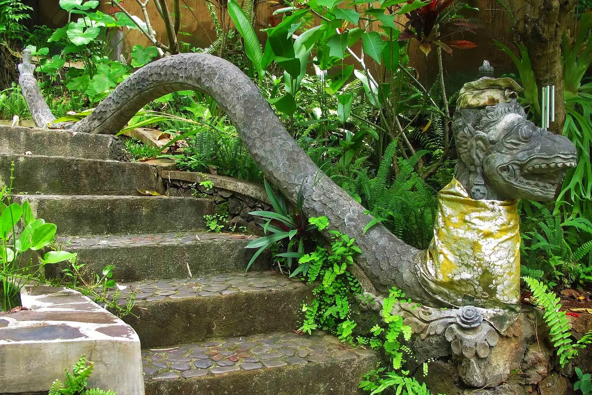 Escaleras de piedra en un jardín con una escultura de un dragón y plantas verdes