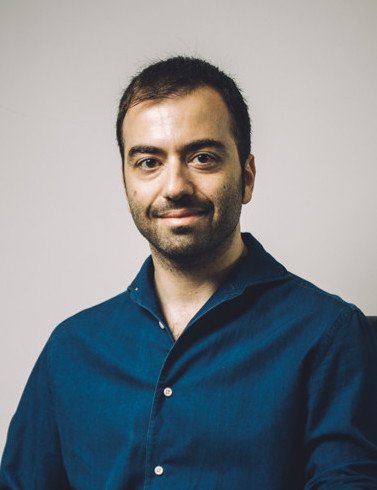 Uomo con capelli corti, barba leggera, che indossa una camicia blu, sfondo neutro.