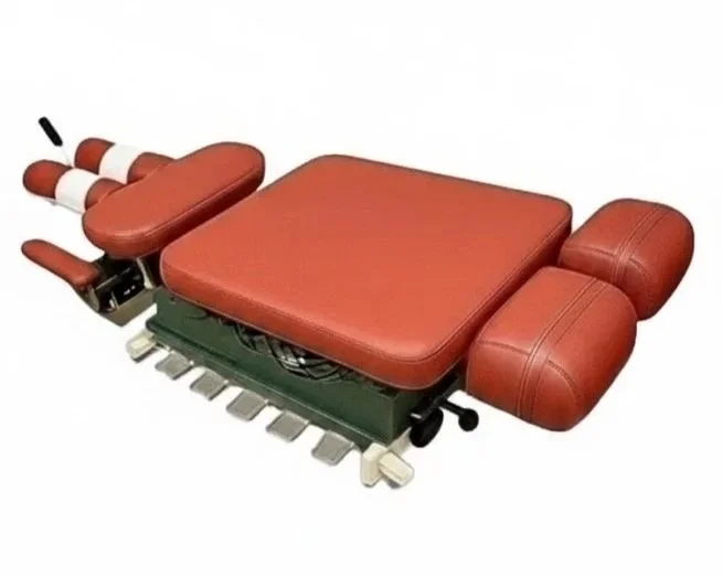 A vintage motorized massage chair with red cushioned seats and armrests, with controls and foot pedals visible underneath.