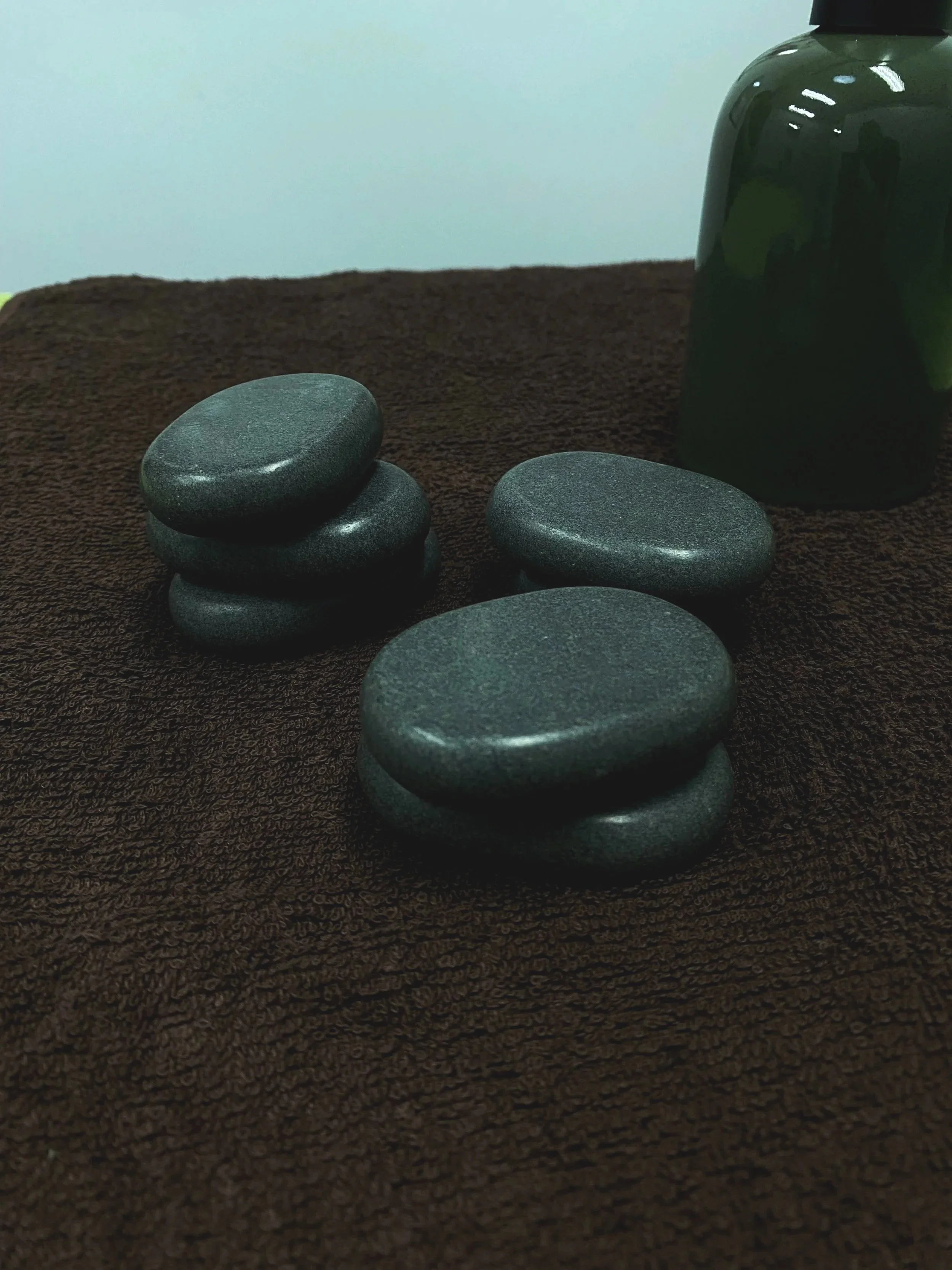A stack of four smooth, black stones on a dark brown textured surface with a dark green vase in the background.