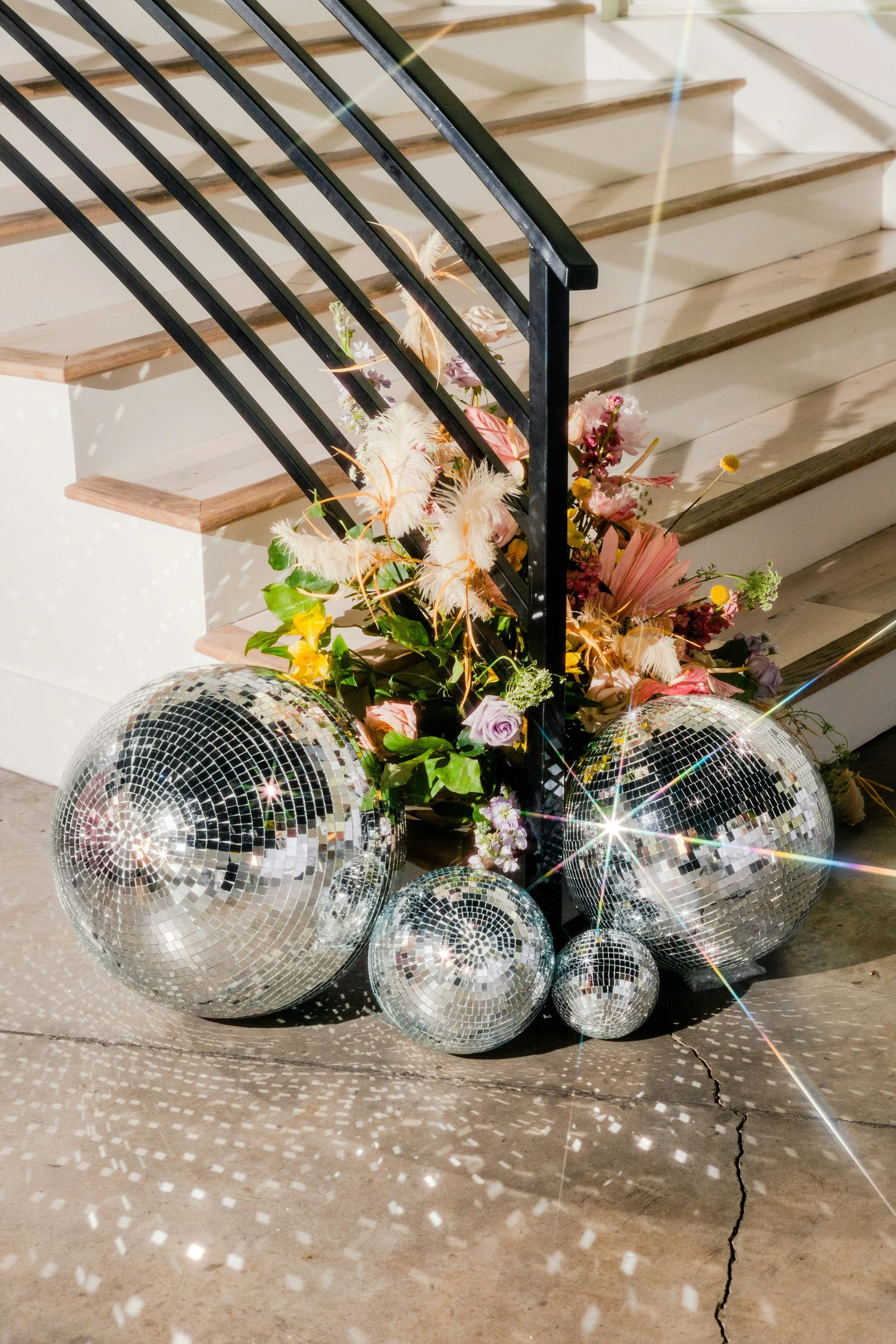 Decorative arrangement of mirror disco balls and assorted pink, purple, and yellow flowers placed at the base of a staircase.