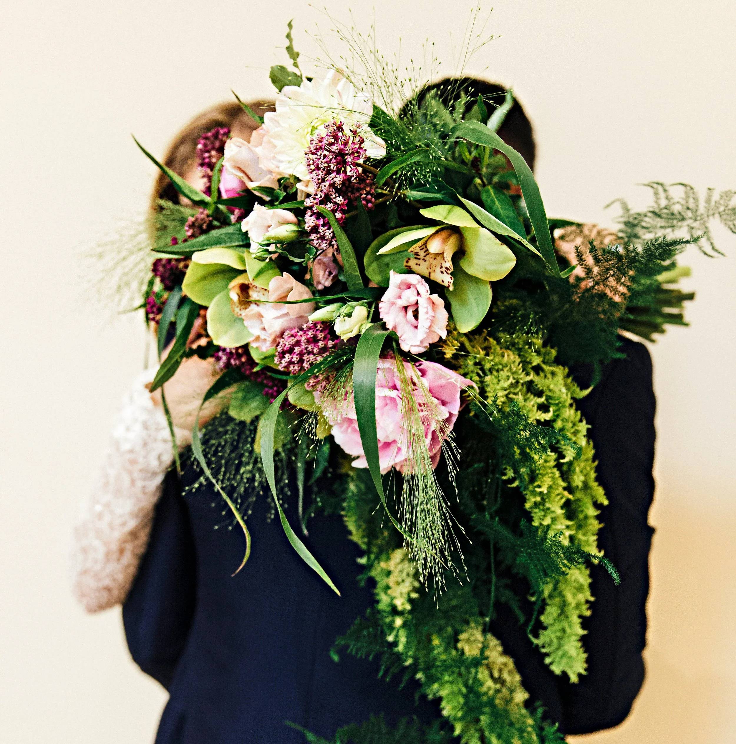 Person holding a large bouquet of assorted pink and purple flowers with green foliage, obscuring their face.