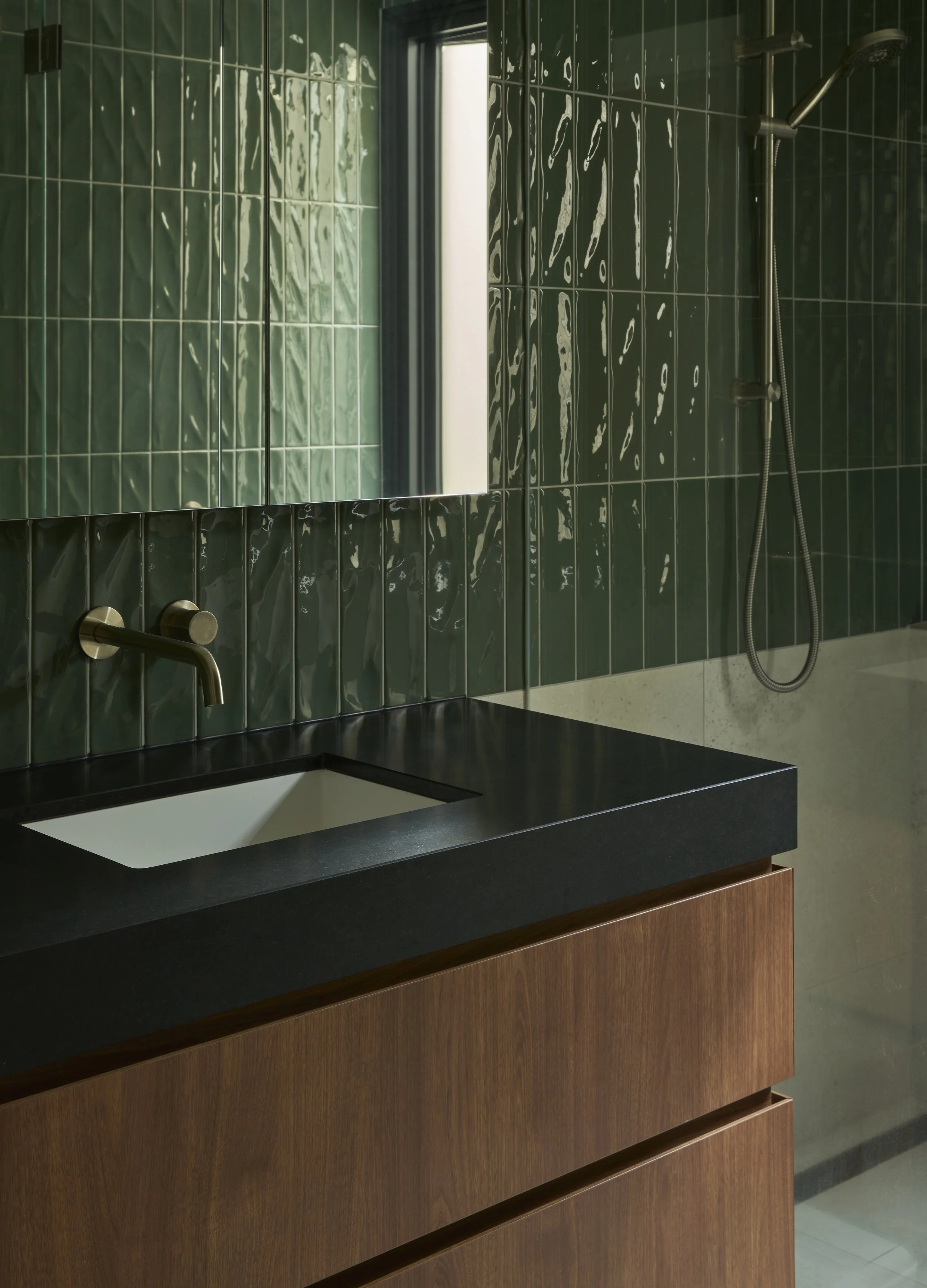 Modern bathroom with green tiled walls, a black countertop sink, wooden cabinet, and a walk-in shower with a handheld showerhead.