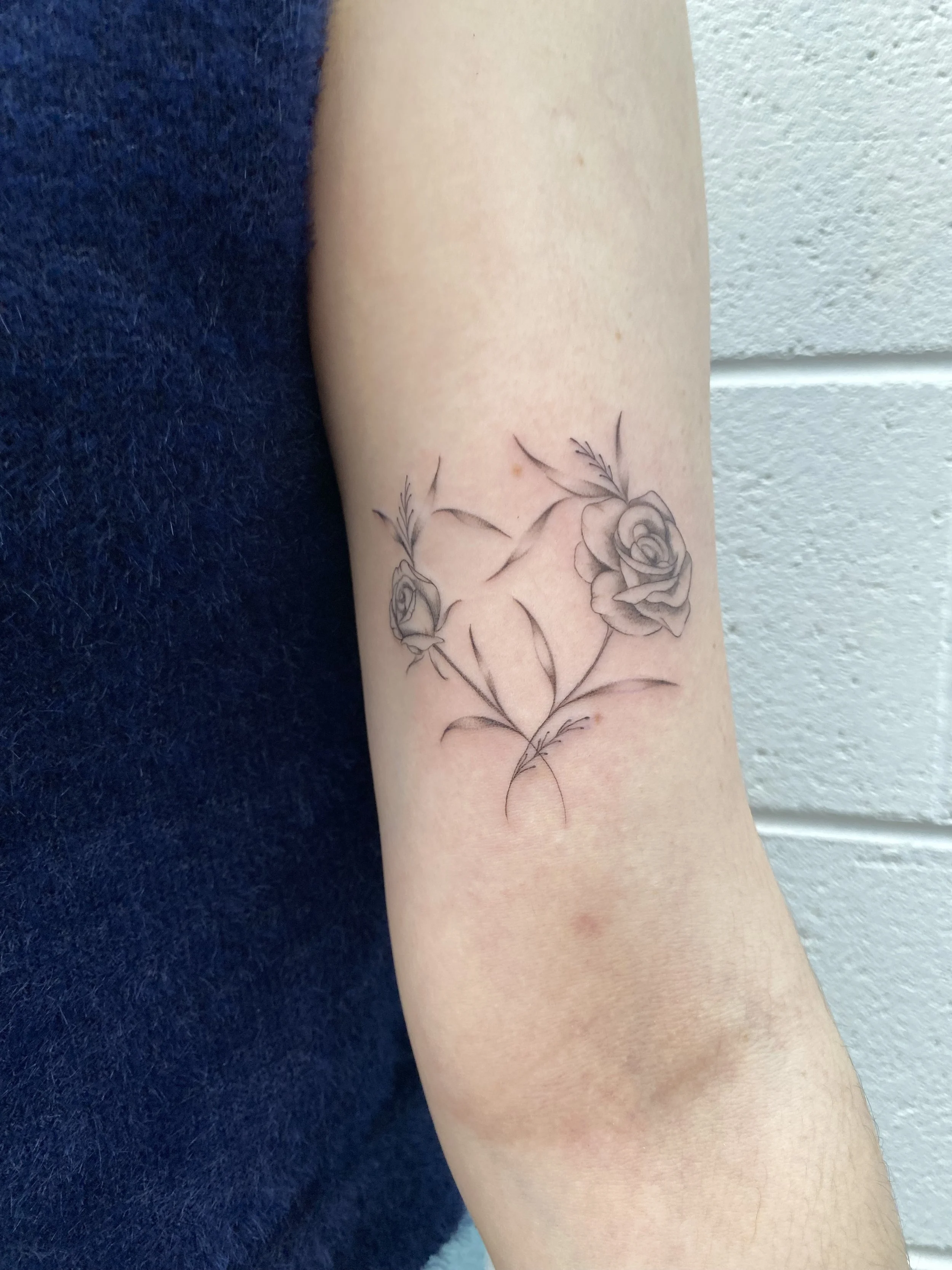 A black and gray floral tattoo of two roses with leaves on a person's inner forearm.