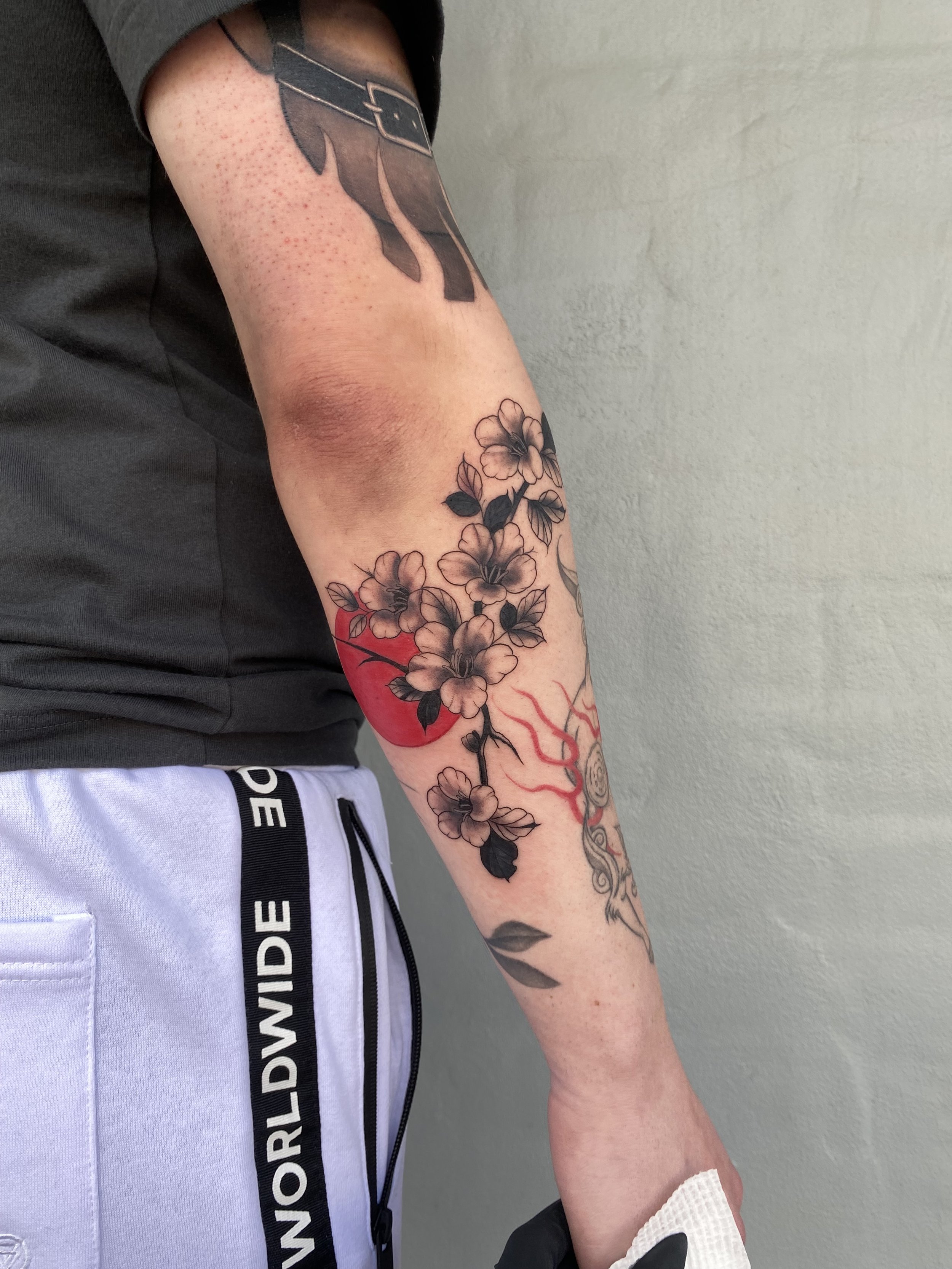 Tattoo sleeve on a person's arm featuring cherry blossoms, a red sun, and other abstract designs.