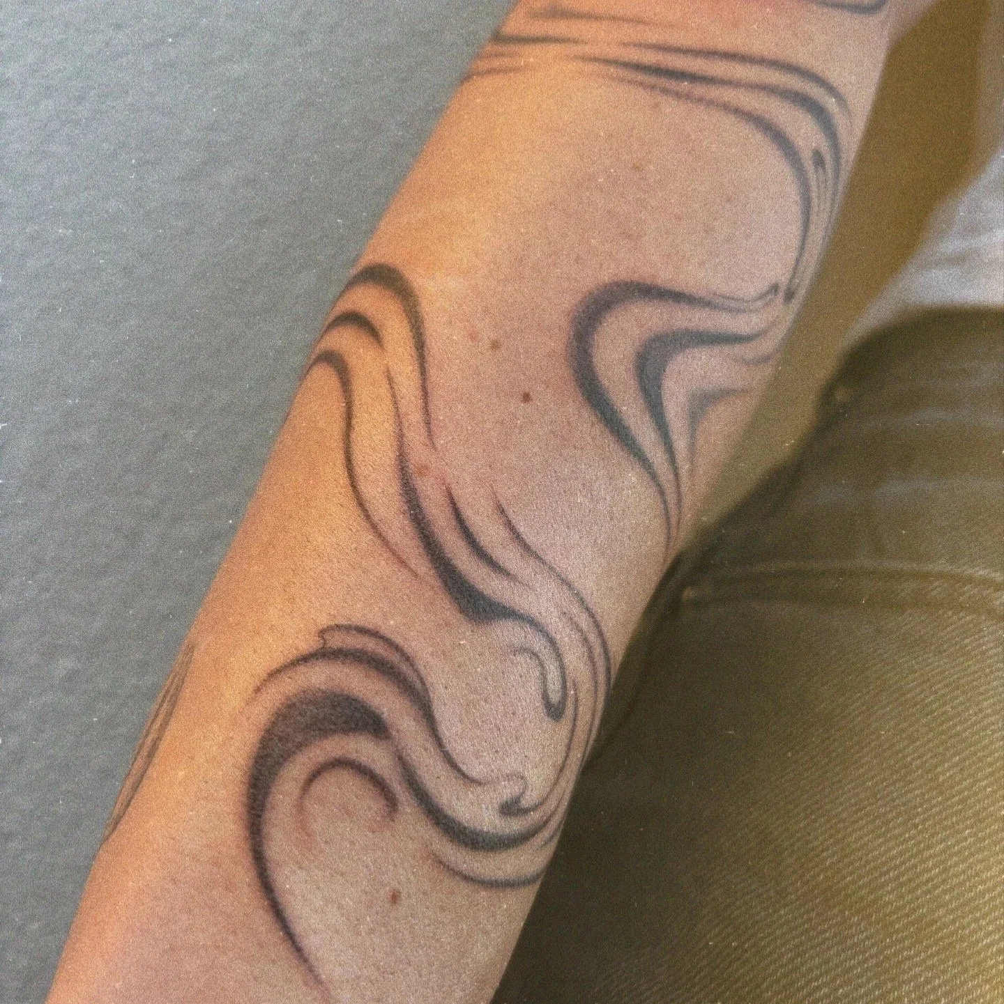 Close-up of a person's forearm with a black ink tattoo of flowing, abstract lines and shapes.