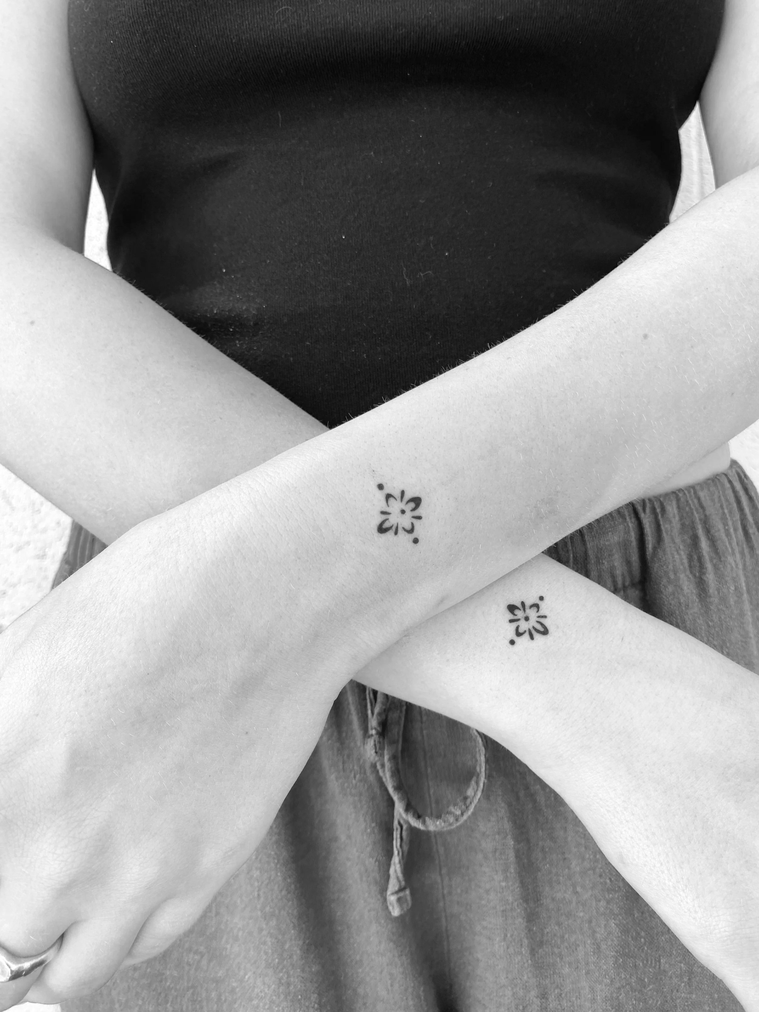 Black and white photo of two crossed arms with matching small flower tattoos on the forearms.