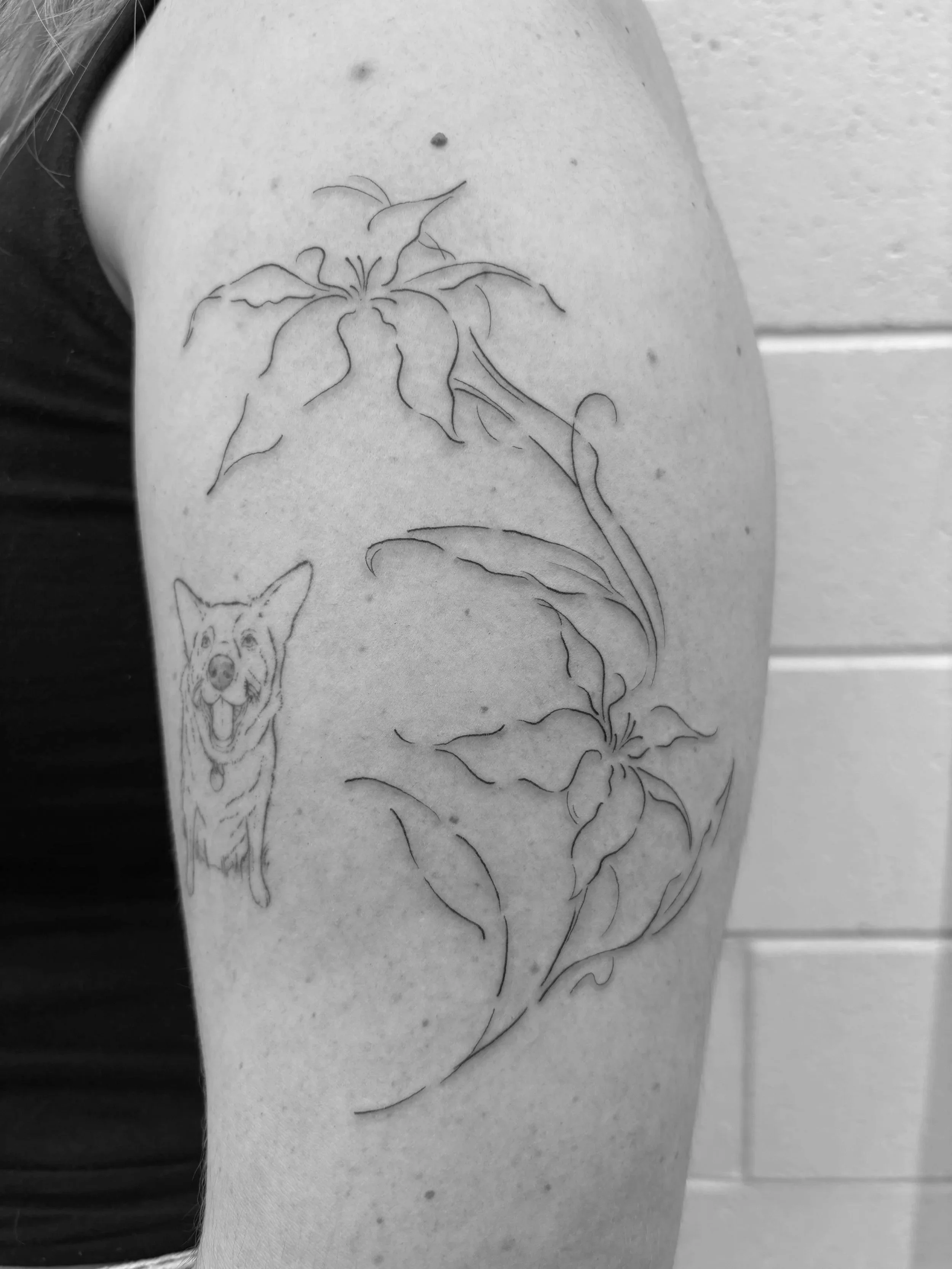 Tattoo of a dog and floral design on a person's arm in black and white.