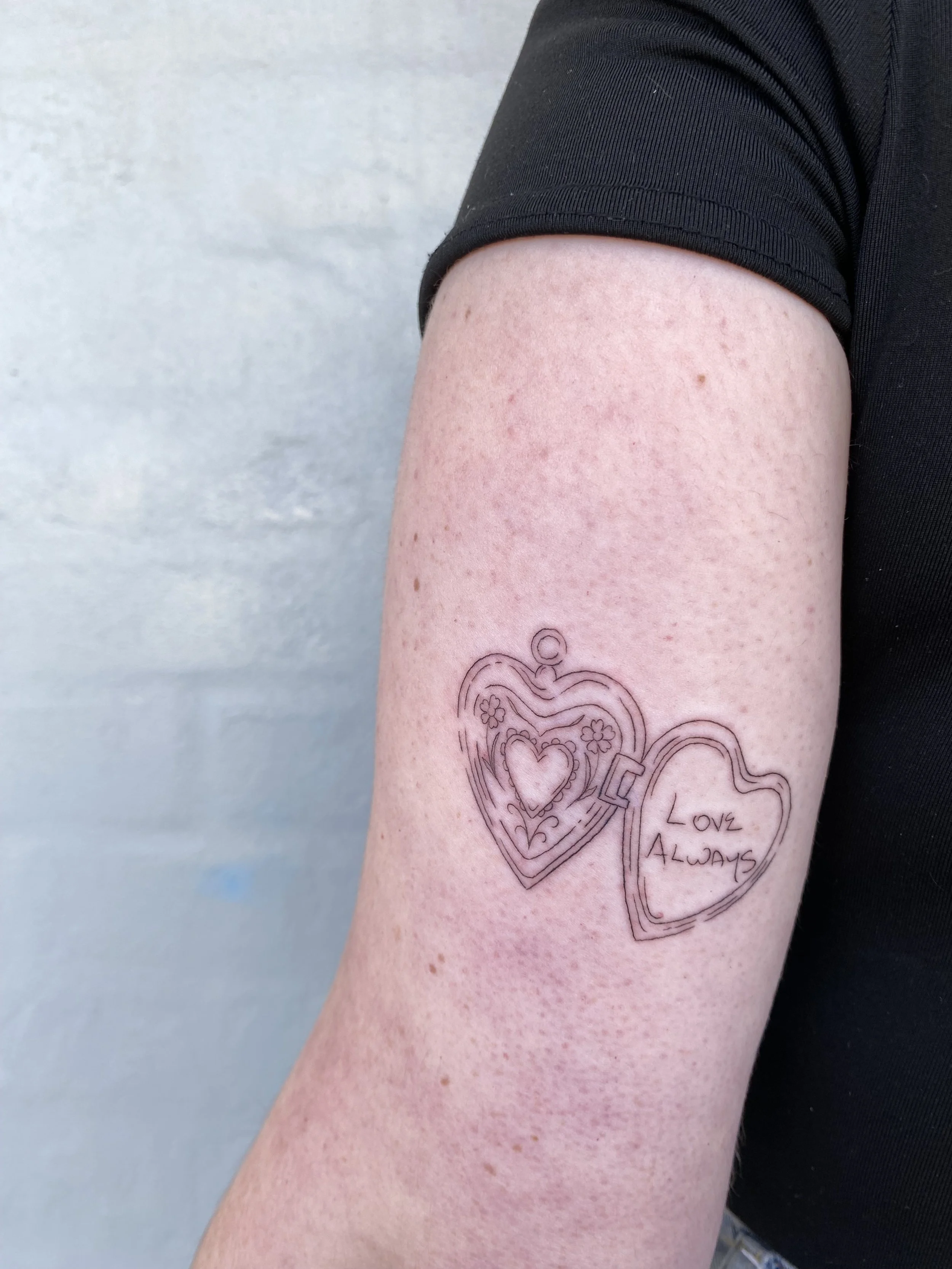 Tattoo of two hearts with floral designs and the words 'Love Always' on a person's upper arm.