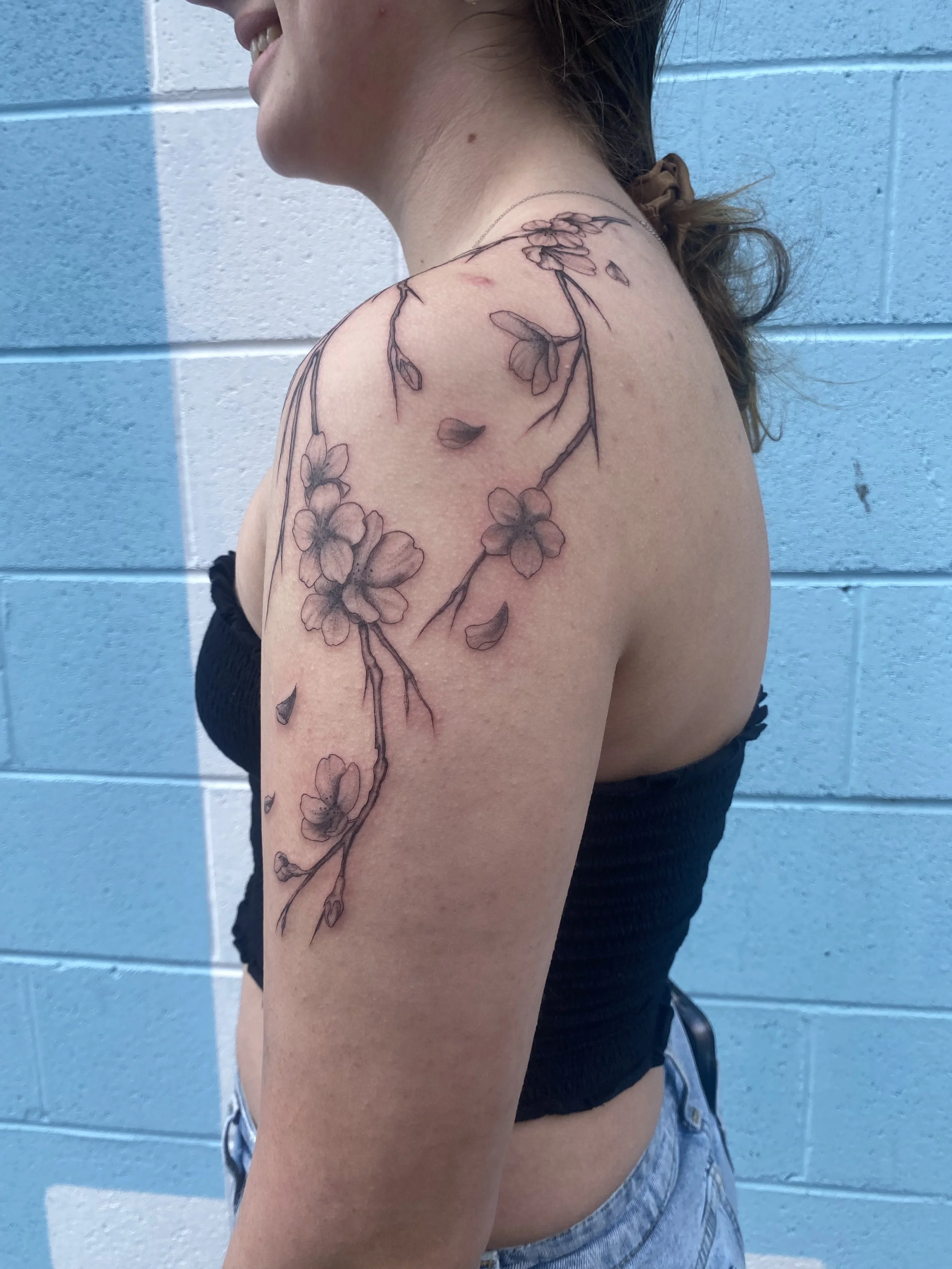 A woman with a floral tattoo on her shoulder and upper arm, standing against a blue and white wall.