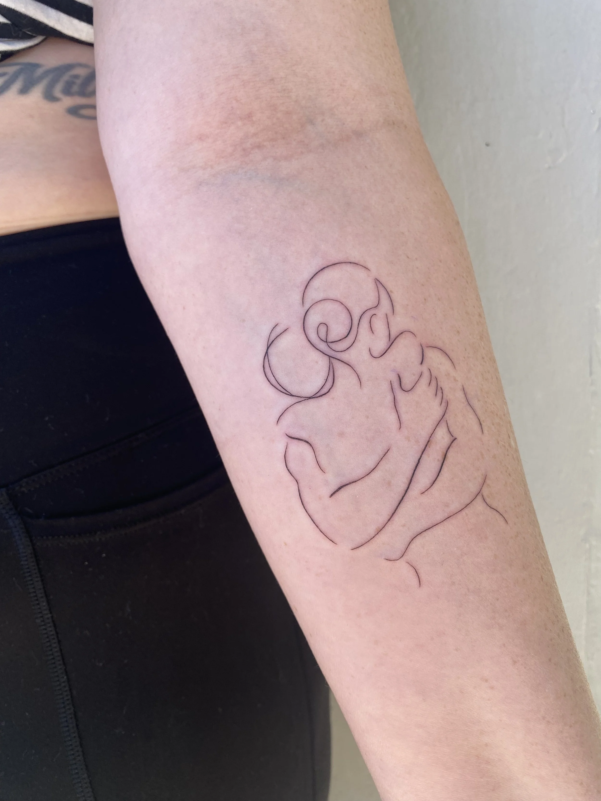 A tattoo outline of a woman holding a baby on the person's arm.