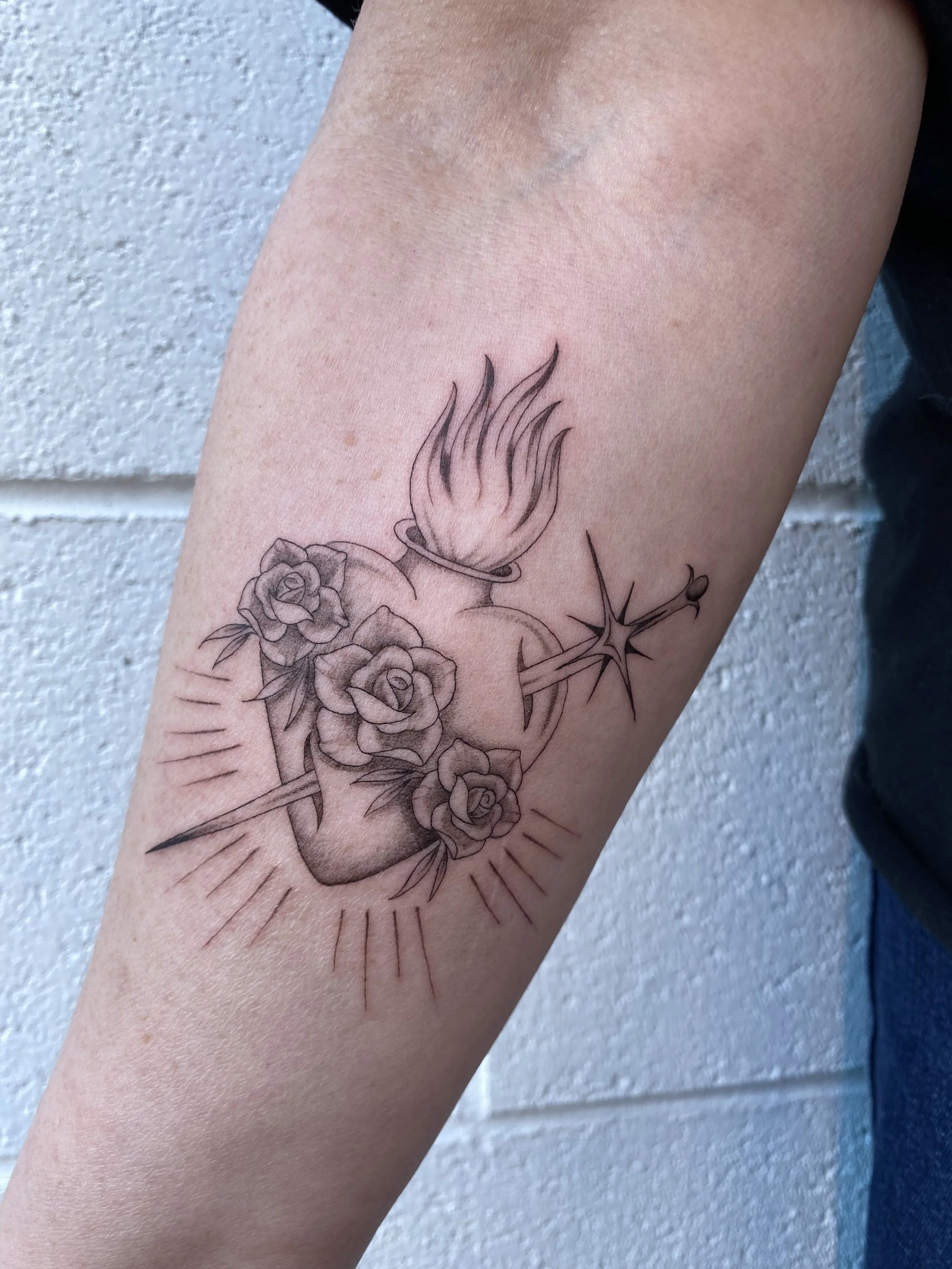 Tattoo of a human heart with roses, a flame, and a stylized starburst.