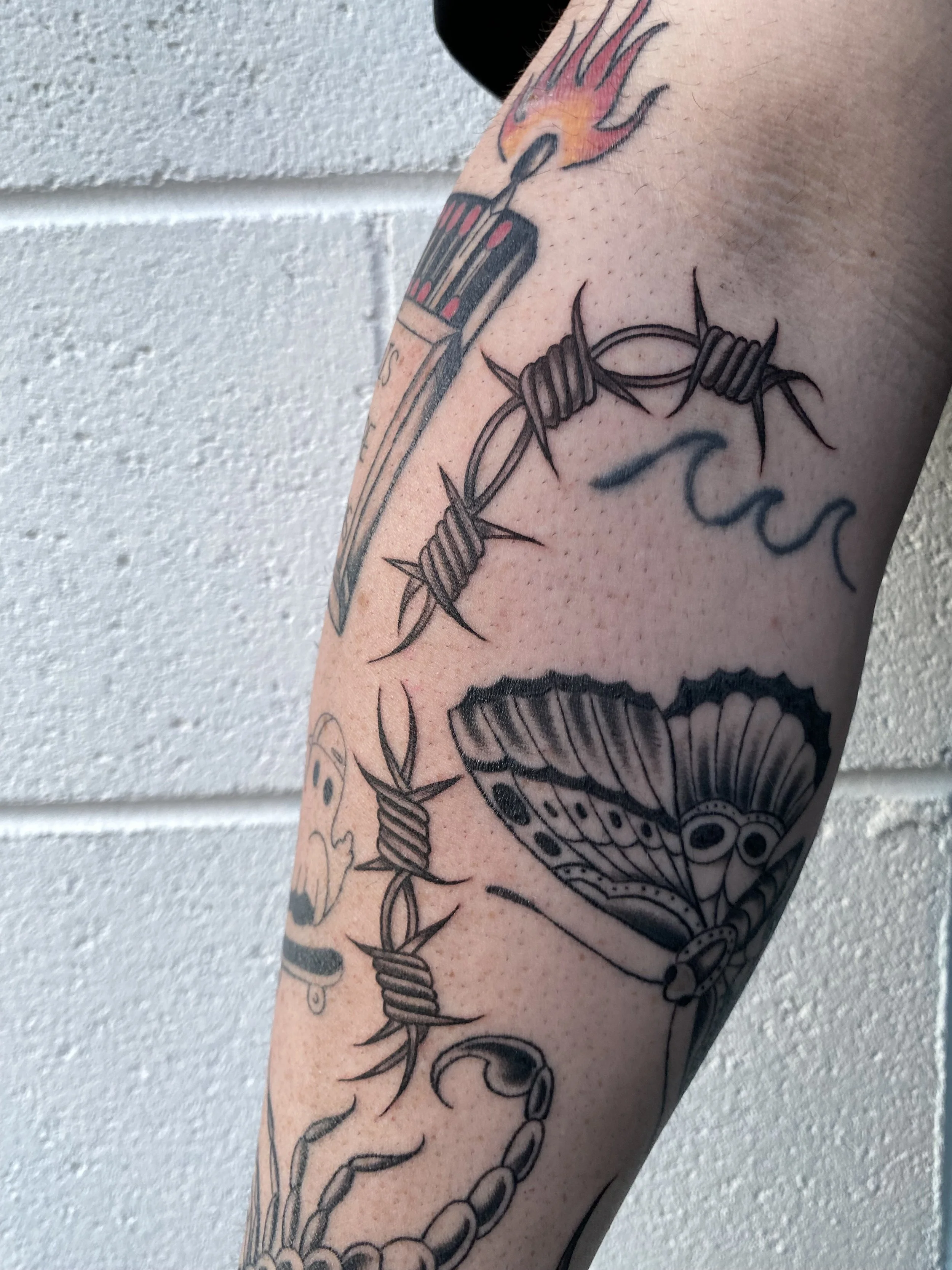 Tattooed arm with a barbed wire circle, butterfly, skull, and fire symbol.