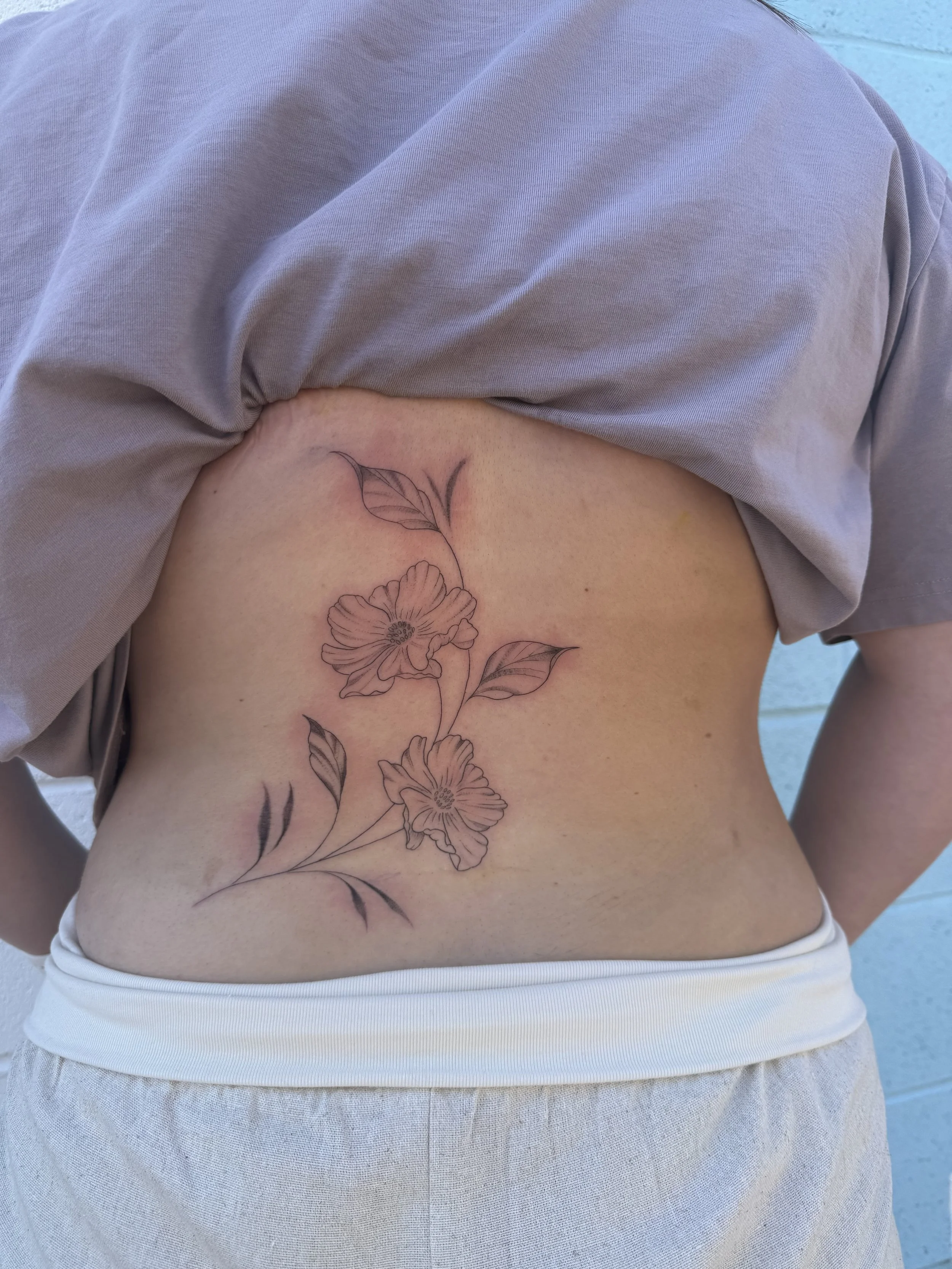 A person's side torso with a floral tattoo featuring two large flowers and leaves.