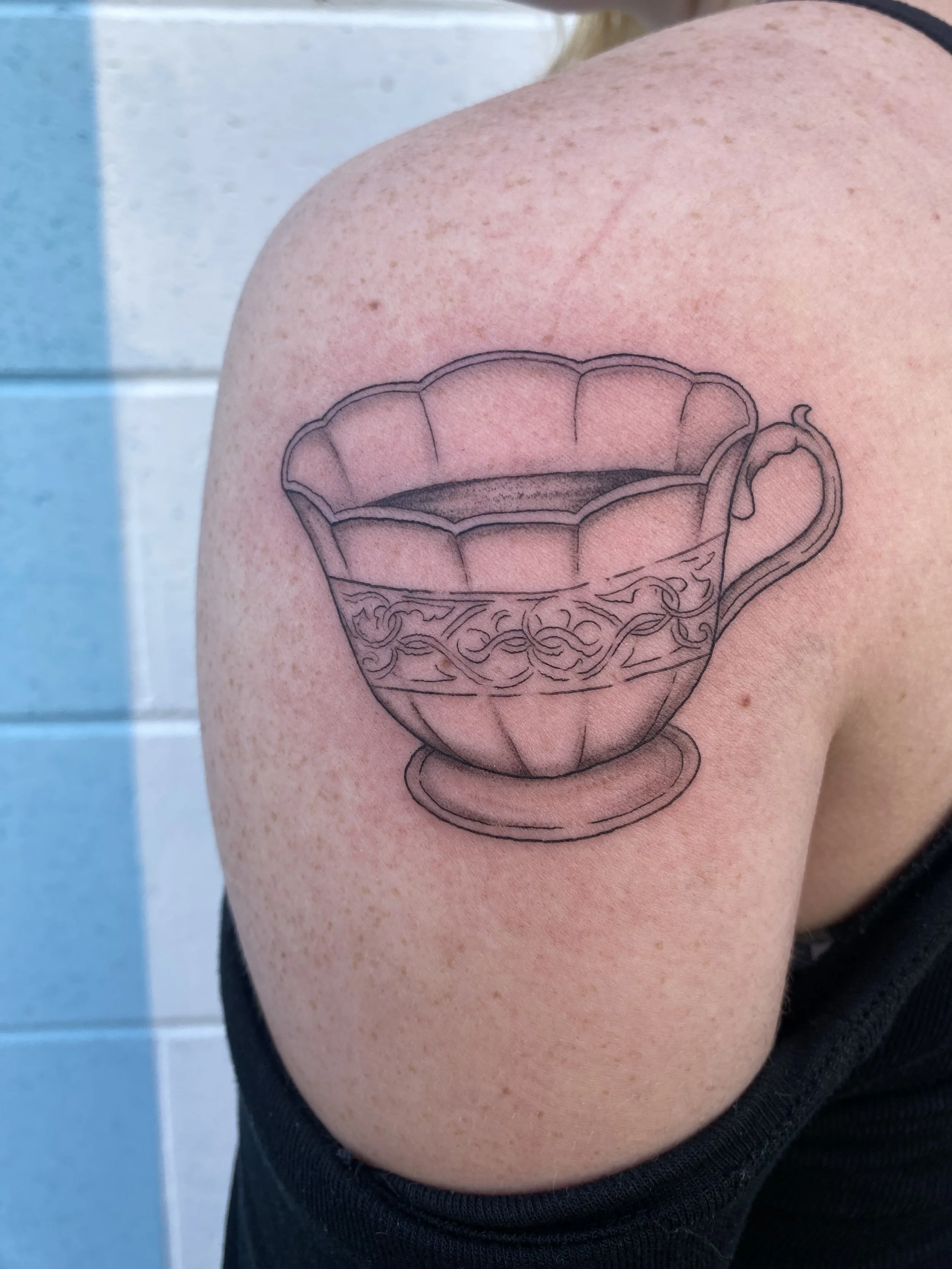Tattoo of a detailed teacup on person's upper arm.
