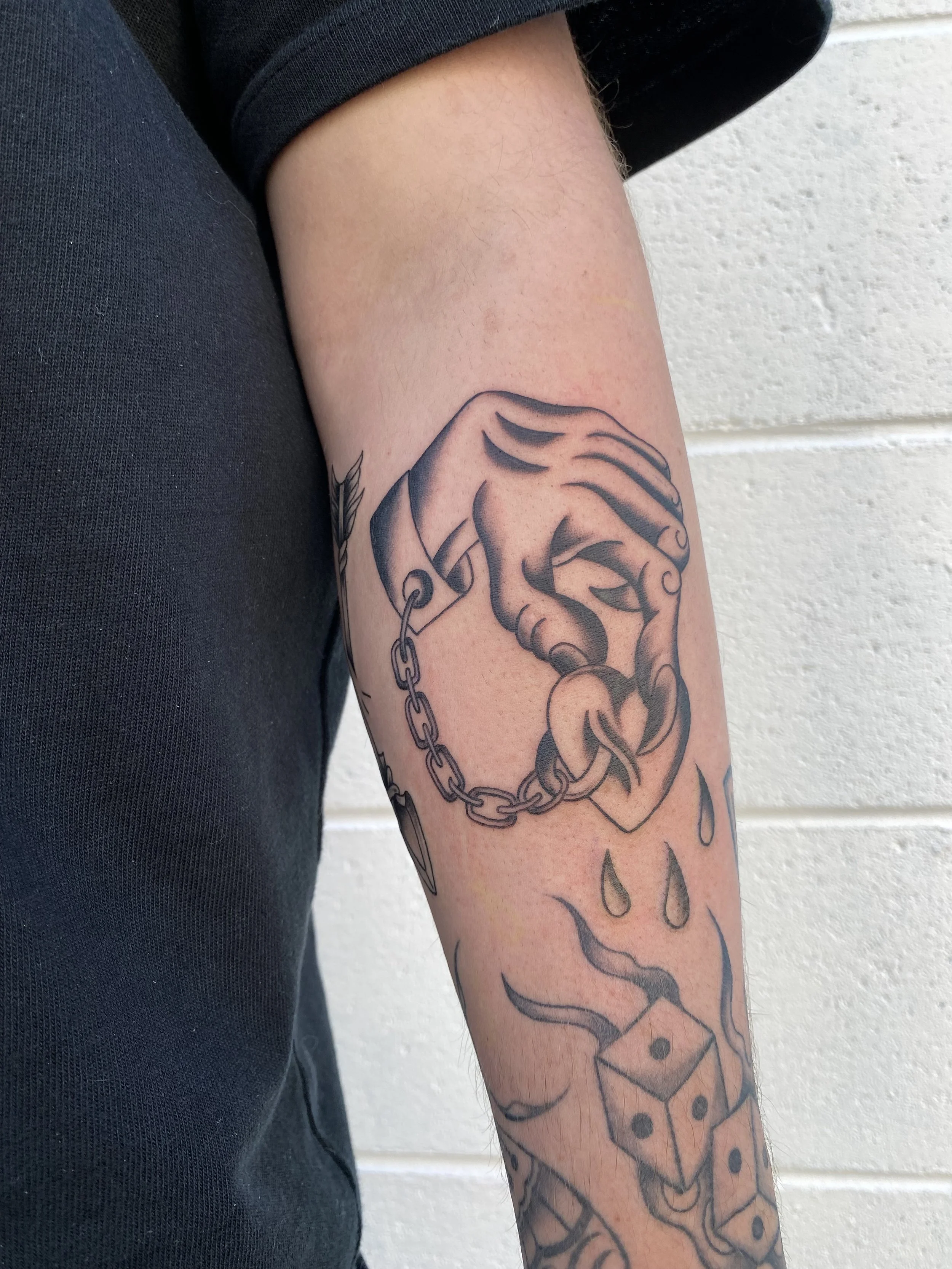 Tattoo of a hand with chains and dice on a person's arm.