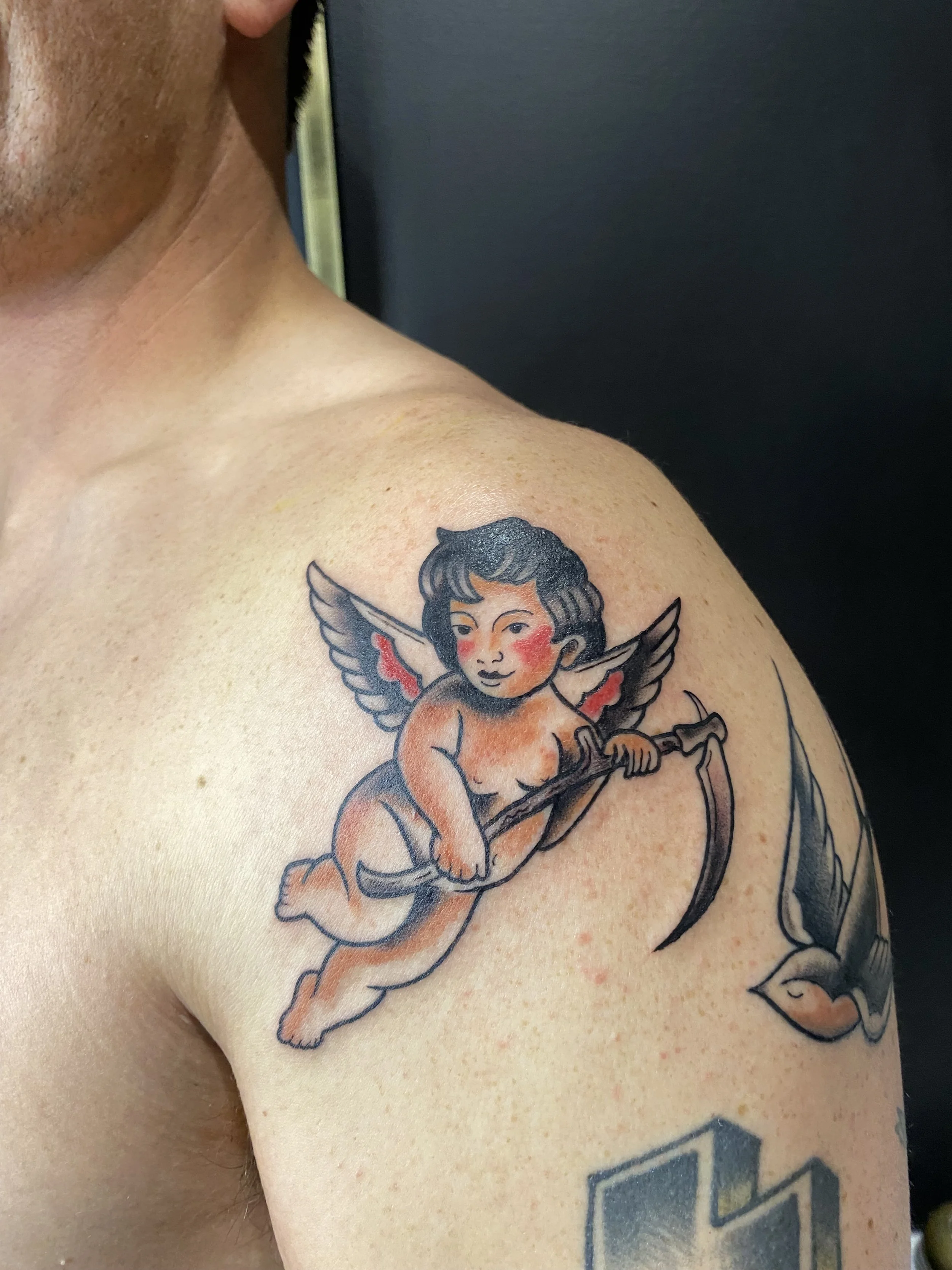 Tattoo of a cherub with wings, holding a bow and arrow, on a person's upper arm.