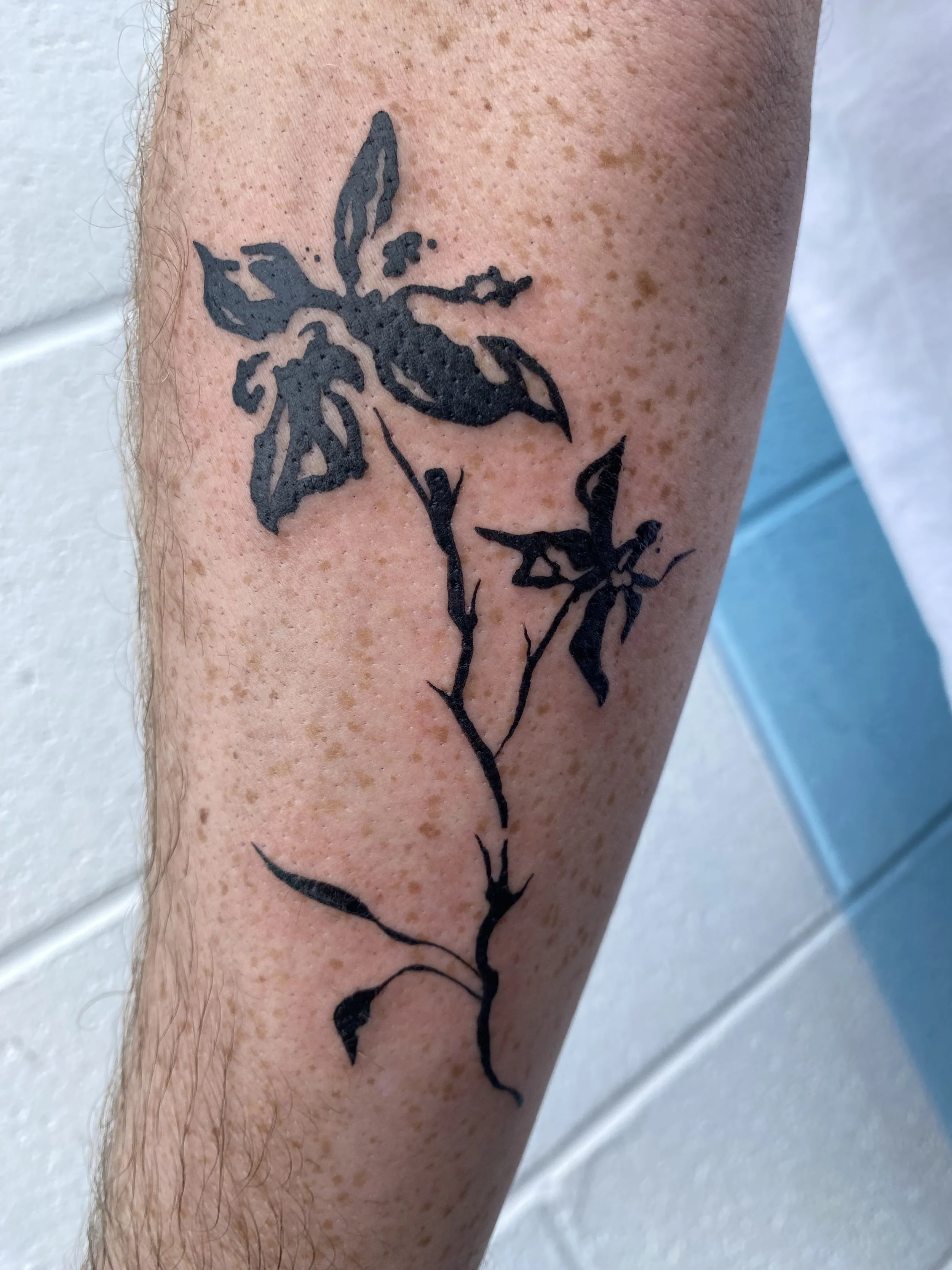 Silhouette tattoo of a flower with leaves on a person's forearm.
