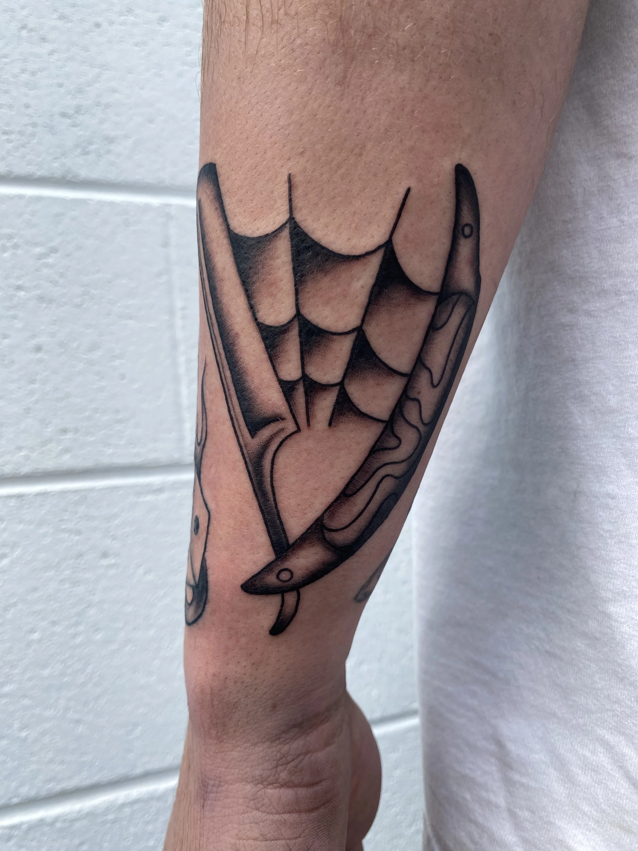 Tattoo of a knife and a realistic spider web on a person's forearm.