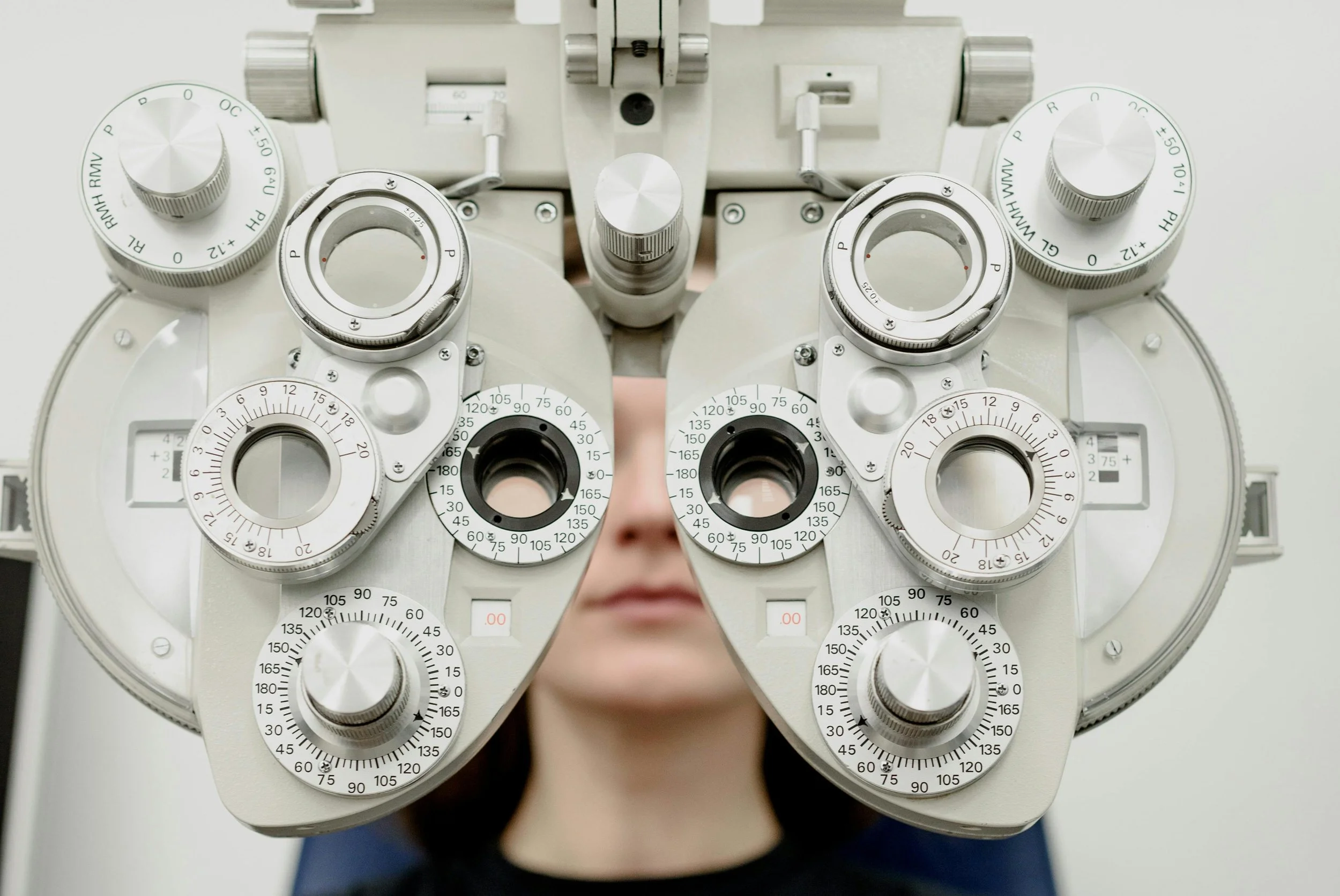 Person looking through a phoropter during an eye exam, with various dials and lenses on the equipment.