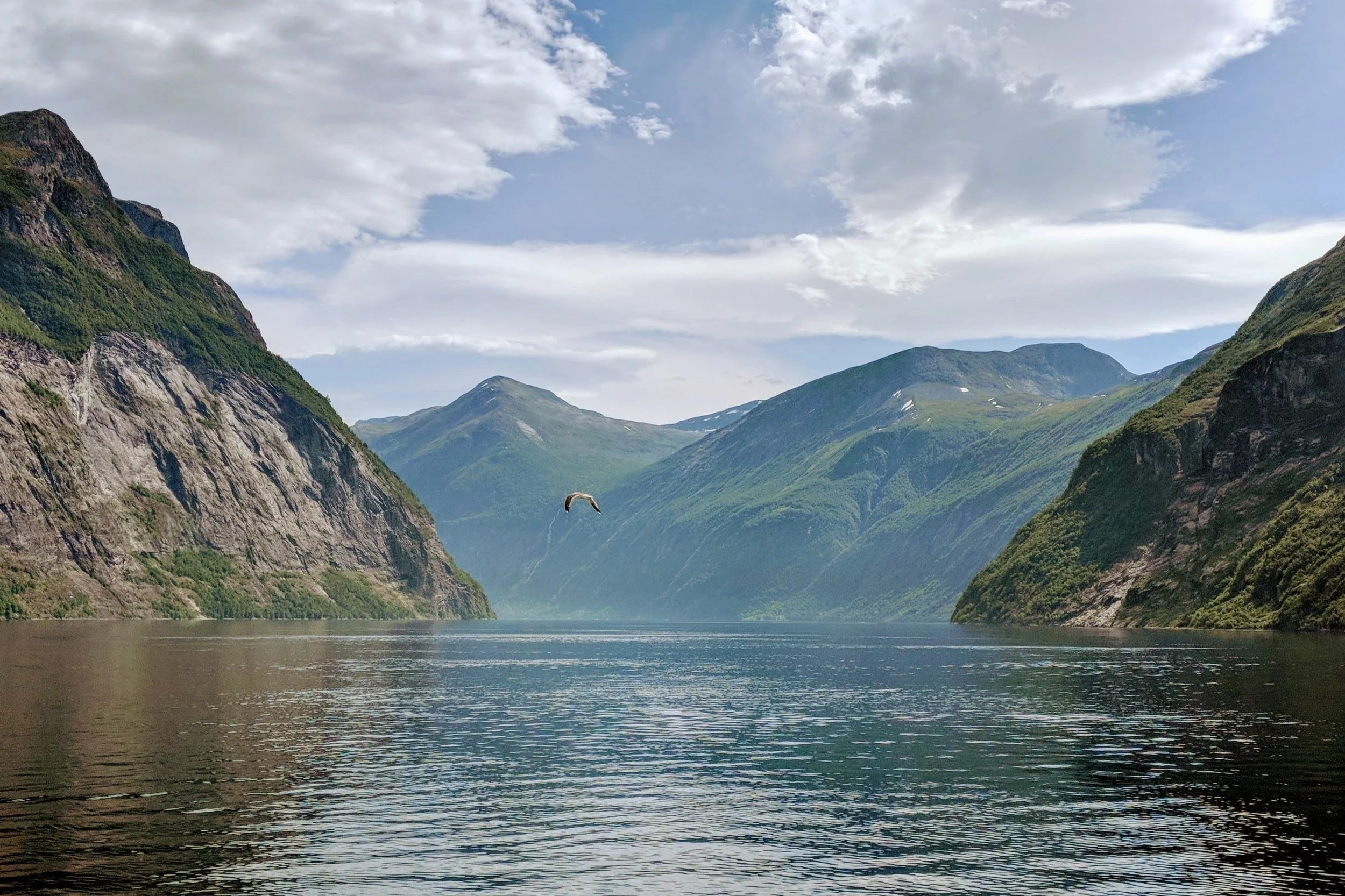 Sommardag ved fjorden med fjell og sol.