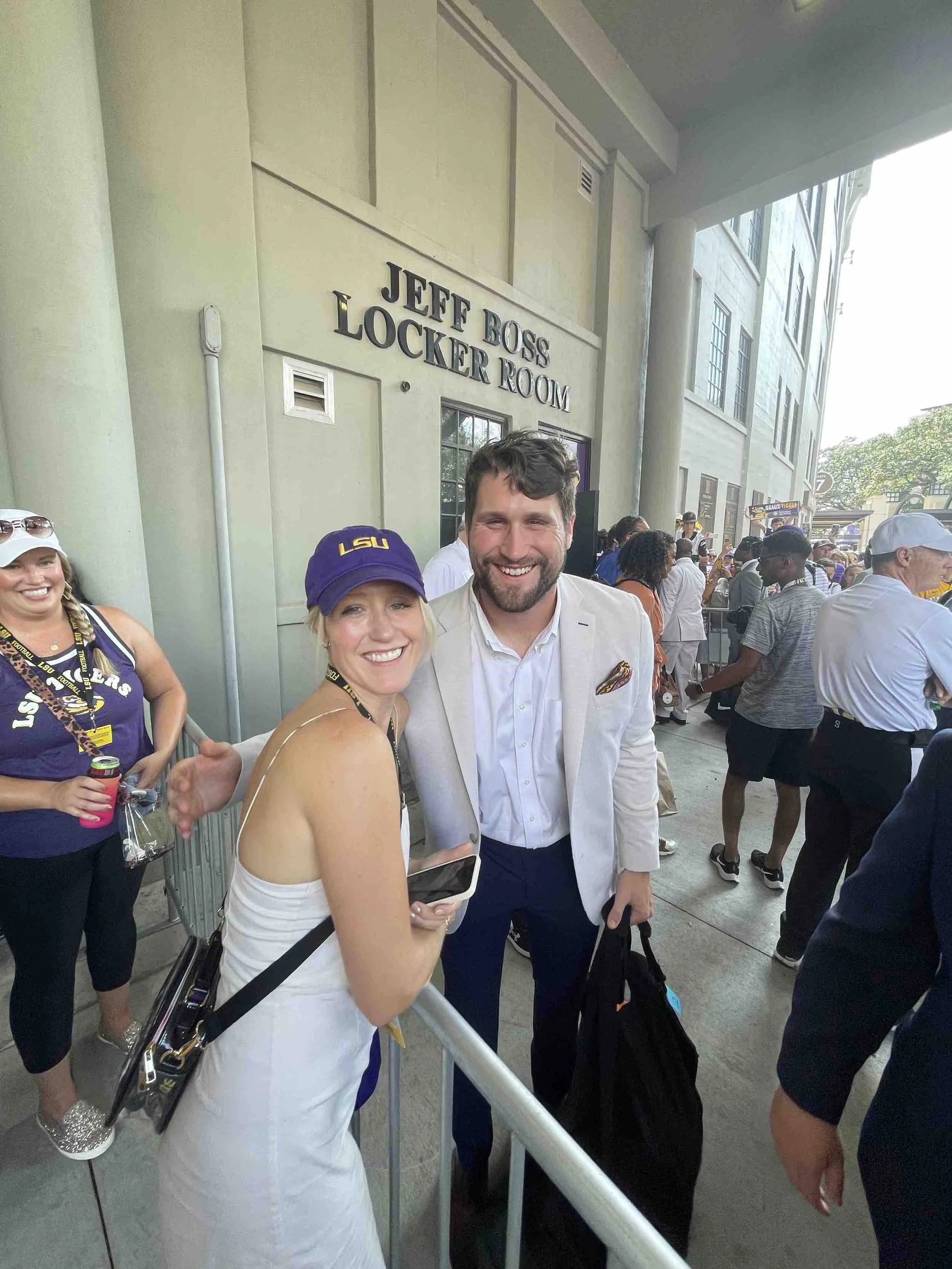 Group of people outside the Jeff Boss Locker Room, smiling and enjoying an event wearing casual and sports attire, with some wearing LSU hats.
